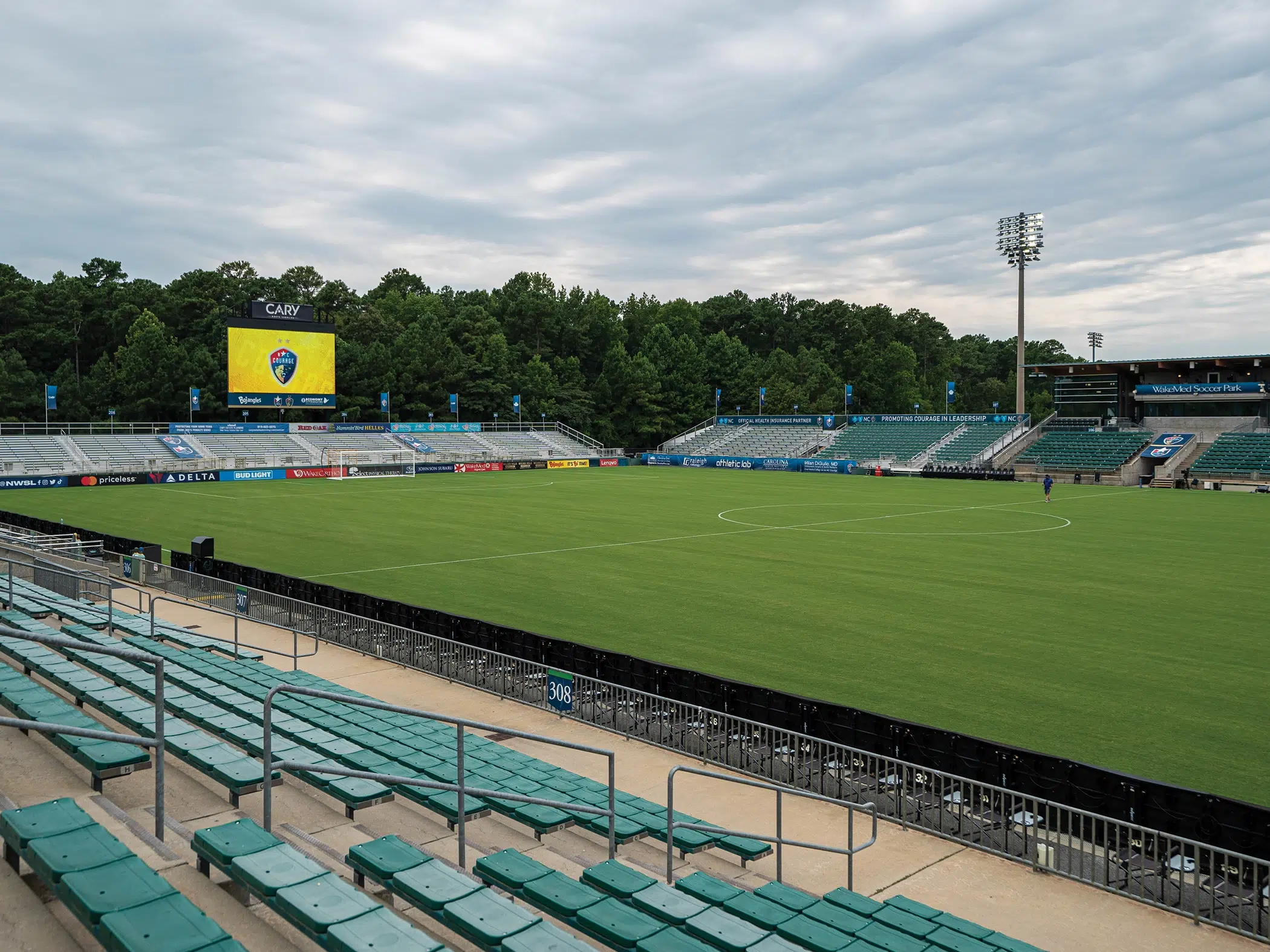 A photo of WakeMed Soccer Park with green bleachers, a video board showing the North Carolina crest, and green, lush trees behind.