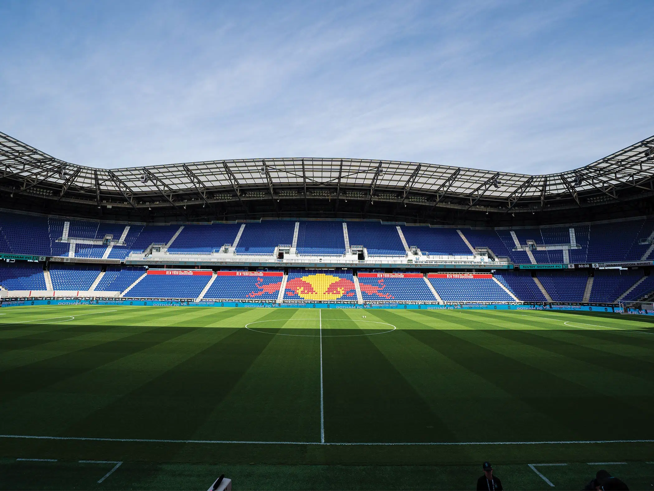 A shot of Red Bull Arena taken at midfield. The blue stands across the field have the Red Bull logo of two red bulls about to collide in front of a yellow sun.