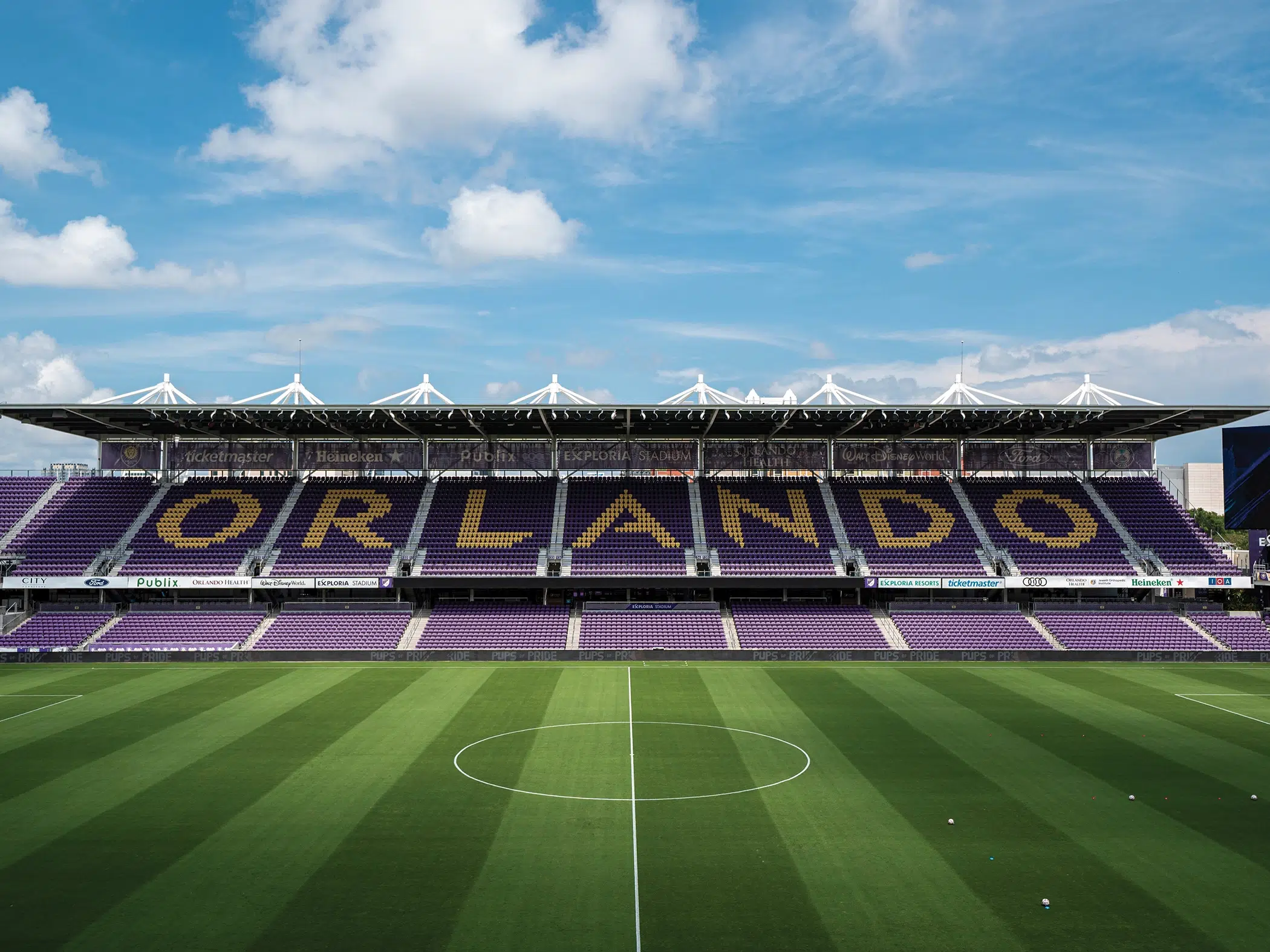 A photo taken from midfield at Exploria Stadium in Orlando, Florida. The seating is purple with the word ORLANDO spelt out in yellow.