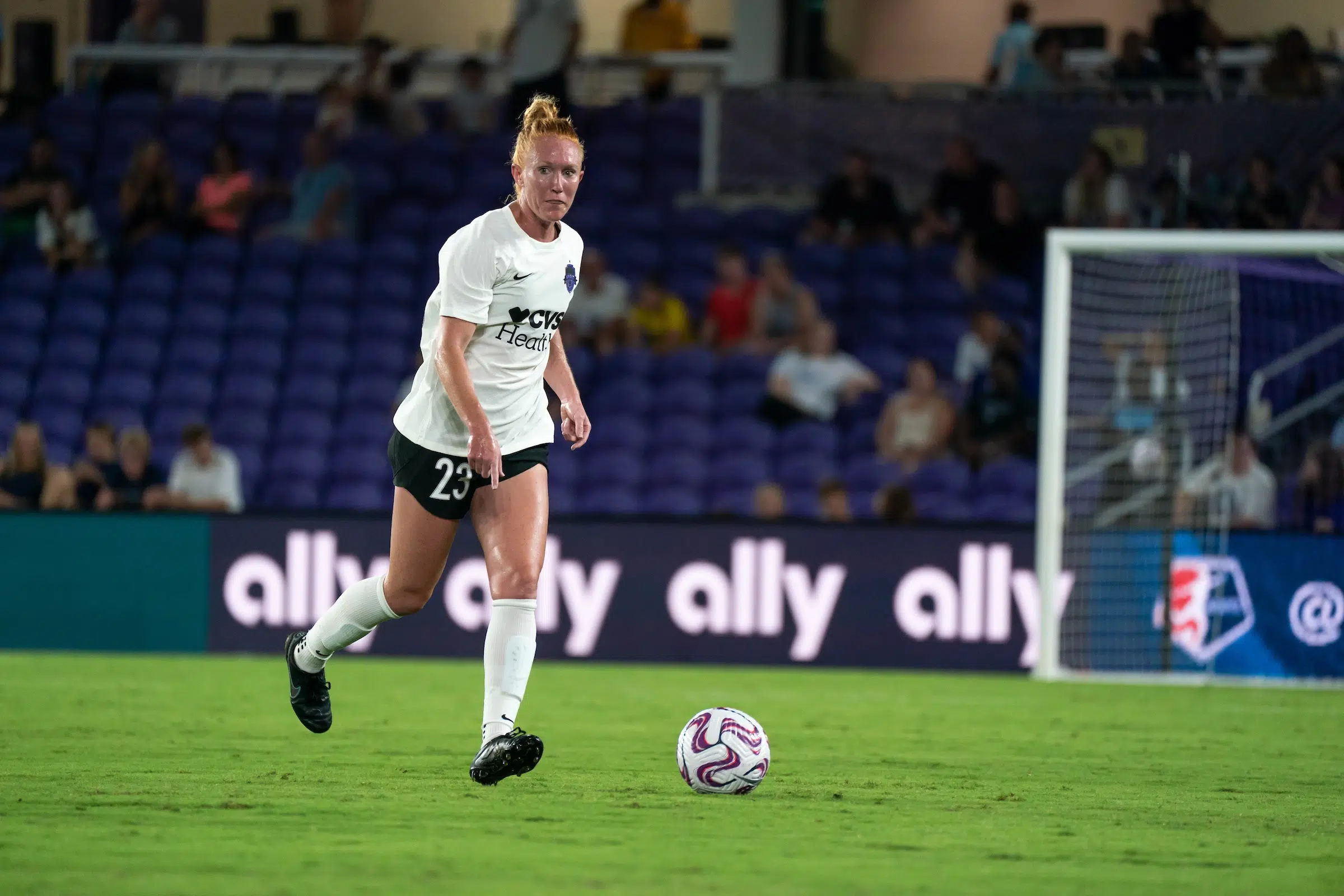 Tori Huster in a white top, black shorts and white socks dribbles a soccer ball.