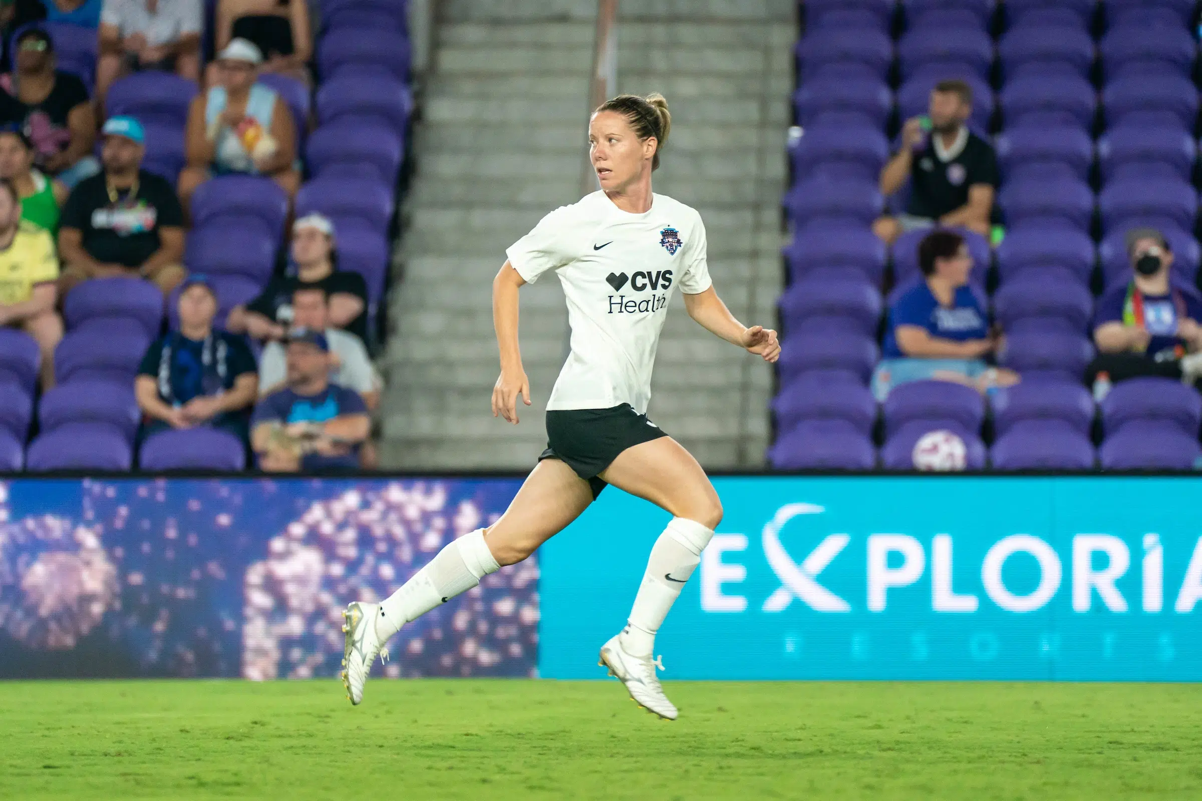 Annaig Butel in a white top and black shorts runs on a soccer field while looking backwards.