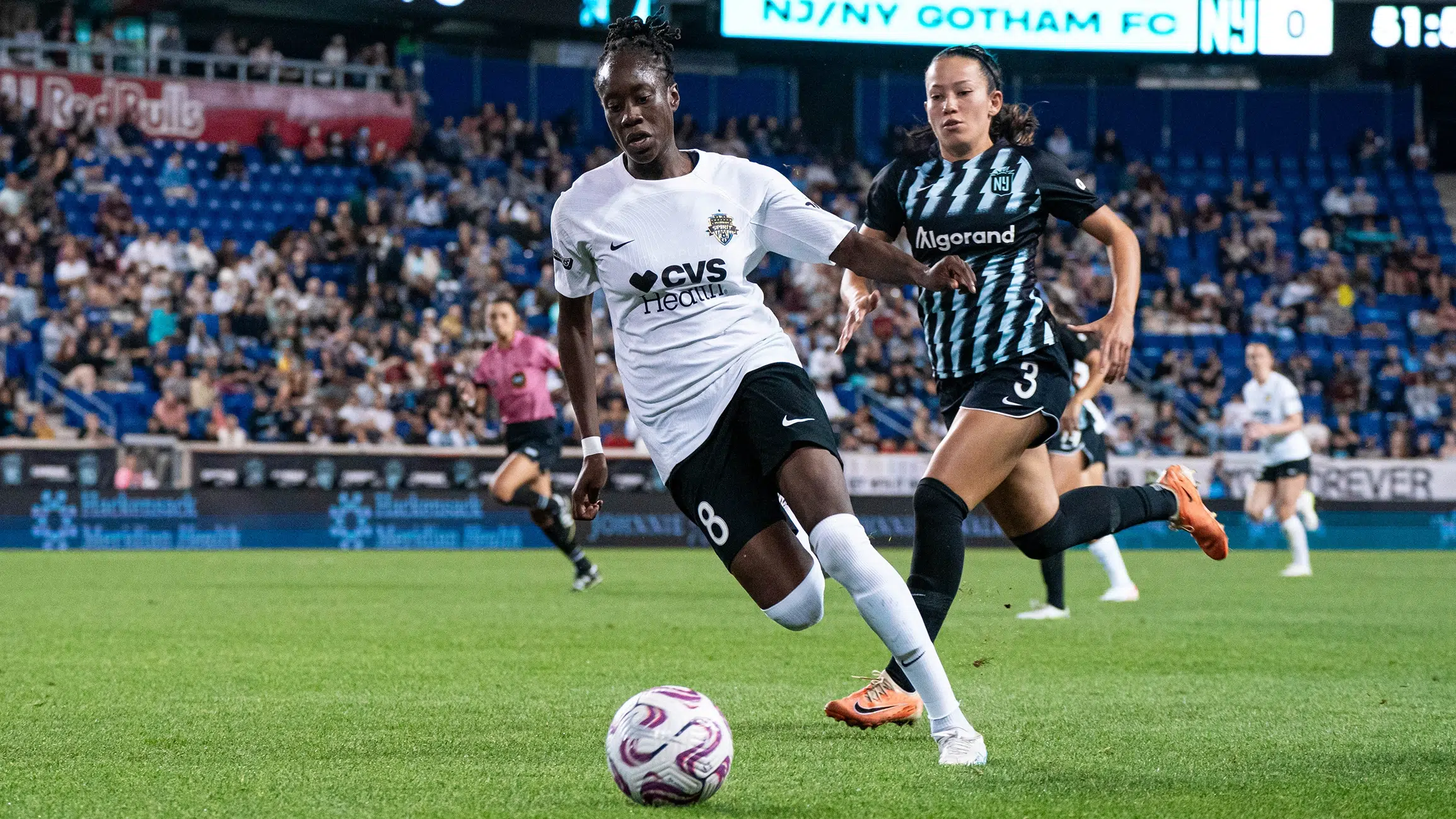 Ouleymata Sarr dribbles the ball past a NJ/NY Gotham defender. She is wearing a white jersey, black shorts, and white socks.