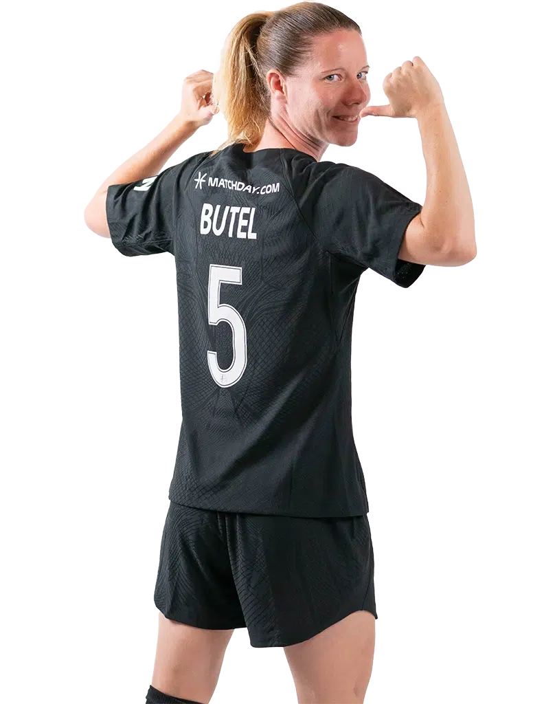 Annaig Butel looks over her shoulder toward the camera with her arms up and thumbs pointing to her name on the back of her black Spirit jersey.