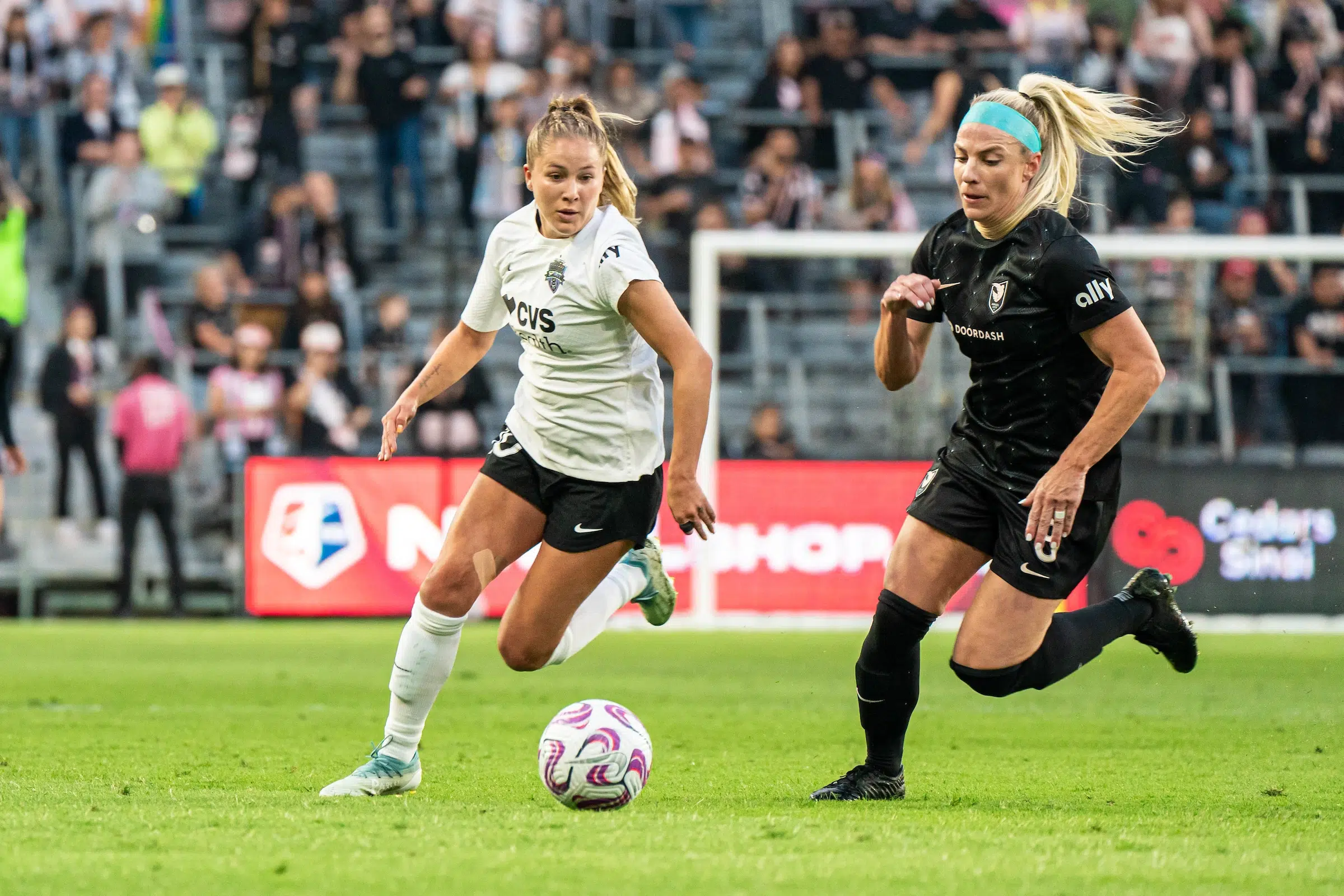Ashley Hatch in a white top, black shorts and white socks attempts to dribble past Julie Ertz in a black uniform.