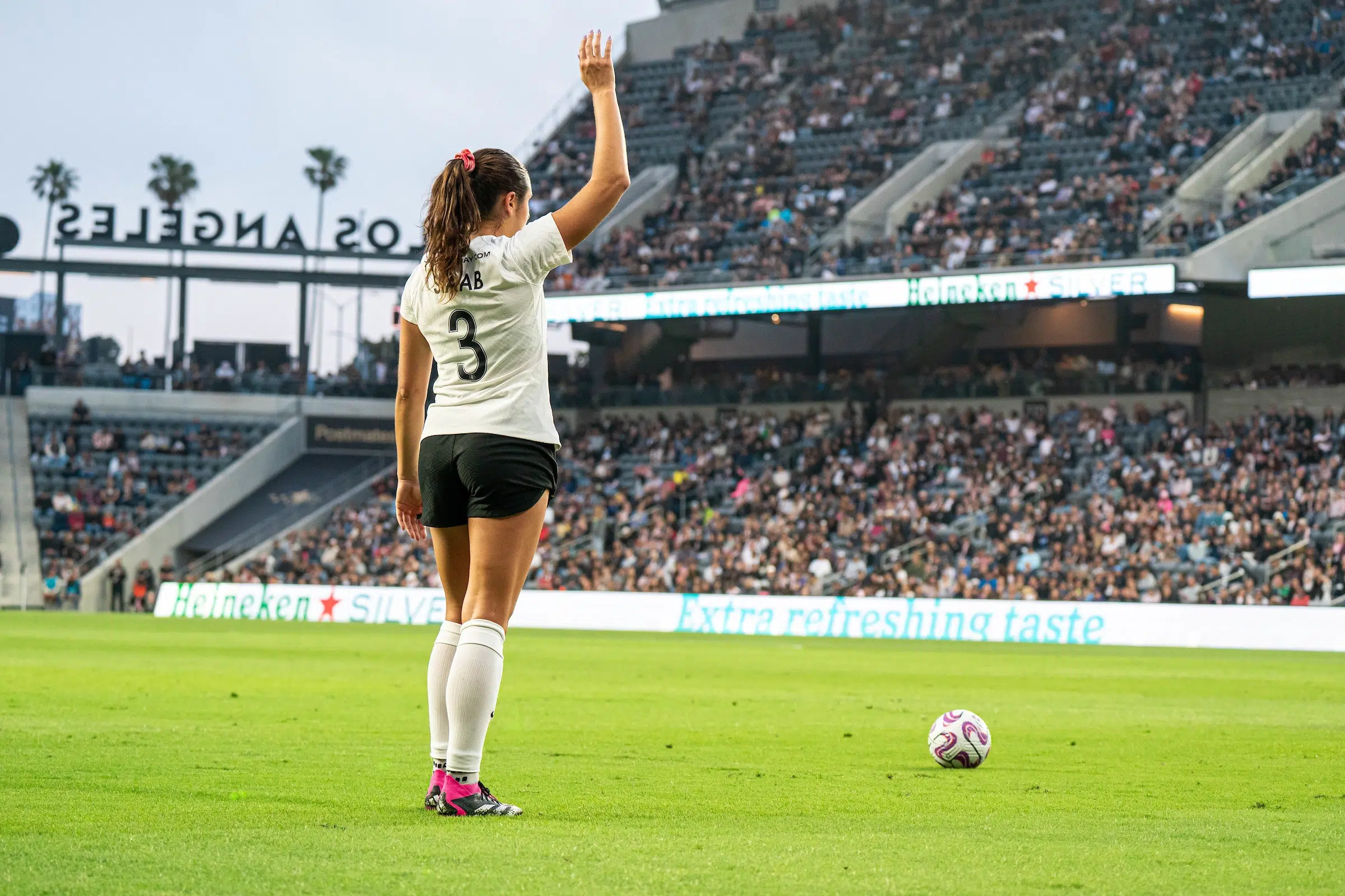 Sam Staab in a white top, black shorts and white socks lifts her hand as she waits to take a free kick.