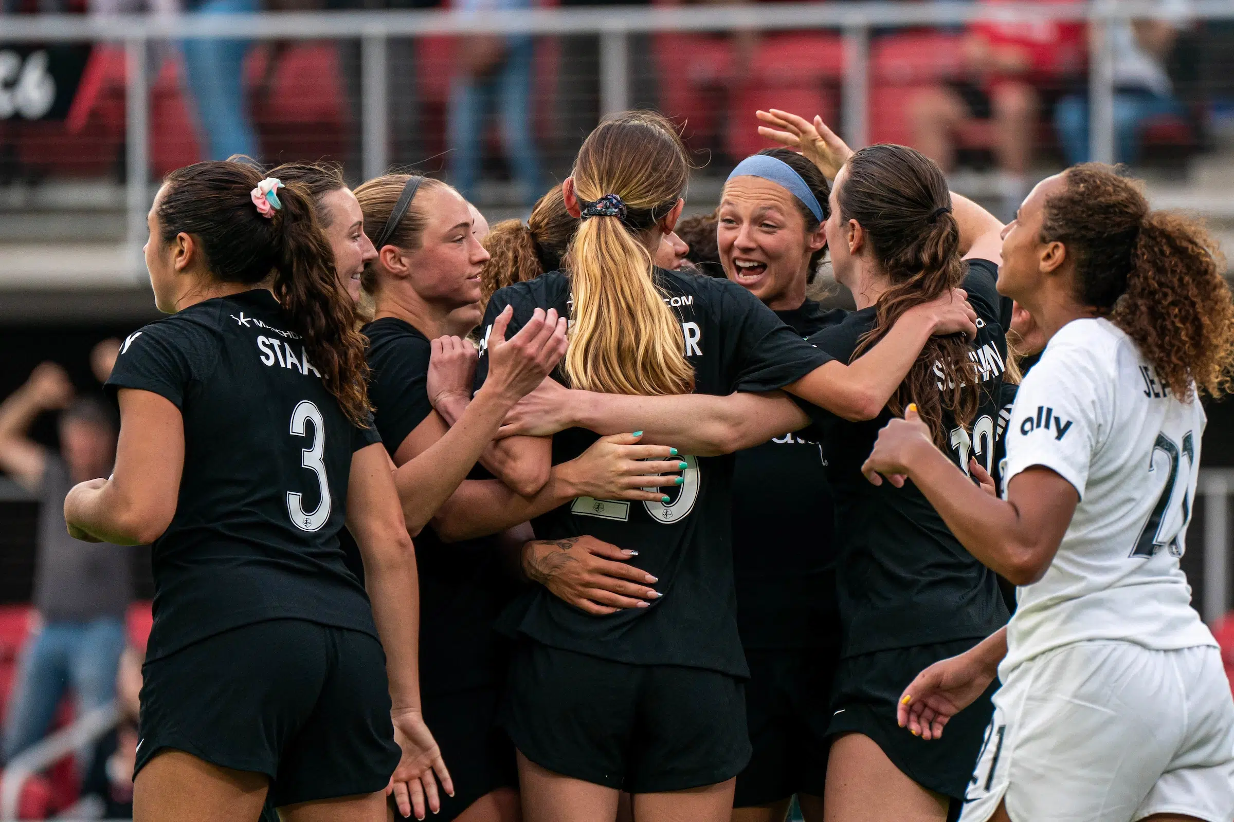 A team of soccer players in all black uniforms hug and celebrate after scoring a goal.
