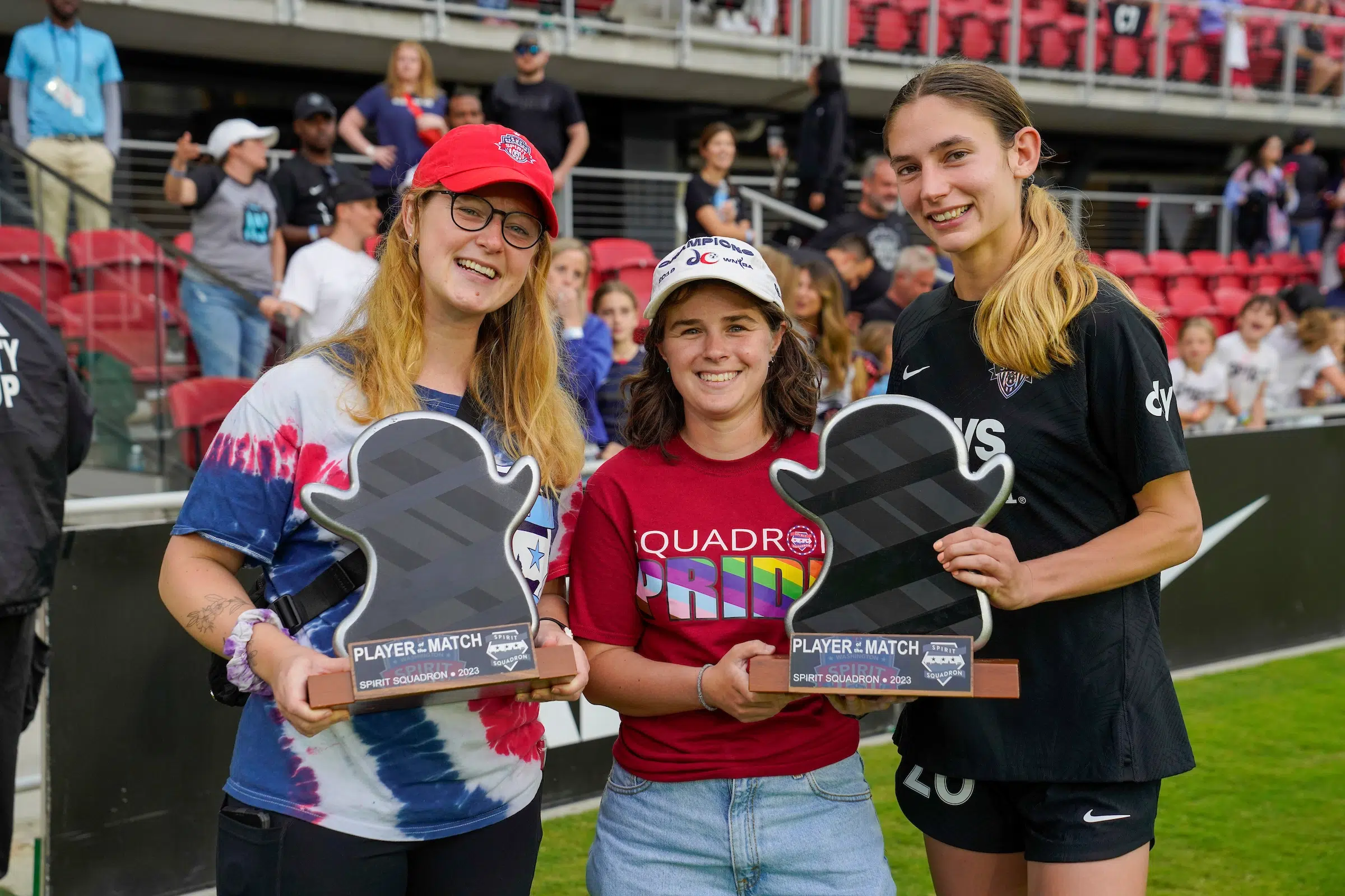 Paige Metayer holds a black, ghost-emoji shaped trophy next to two fans from the Spirit Squadron.