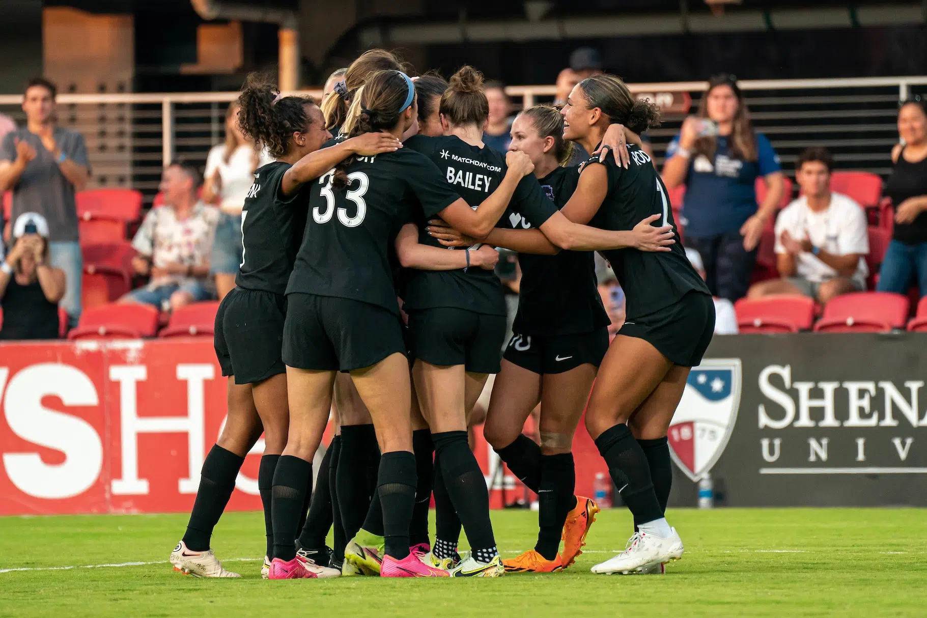 A group of soccer players in all black uniforms form a group hug in celebration of a goal.