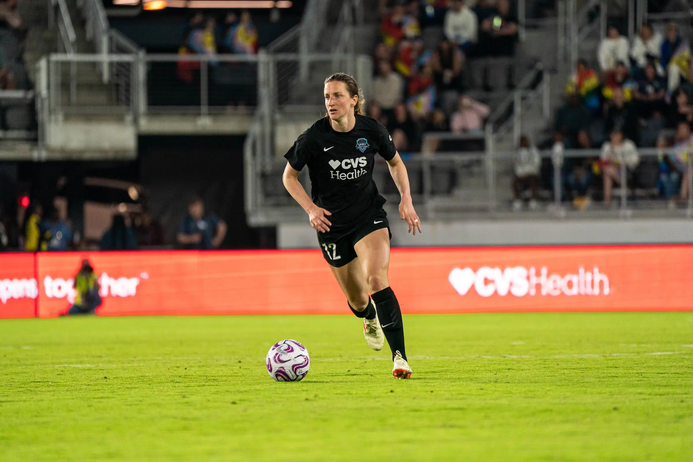 Andi Sullivan in an all black uniform dribbles a soccer ball on a bright green field.
