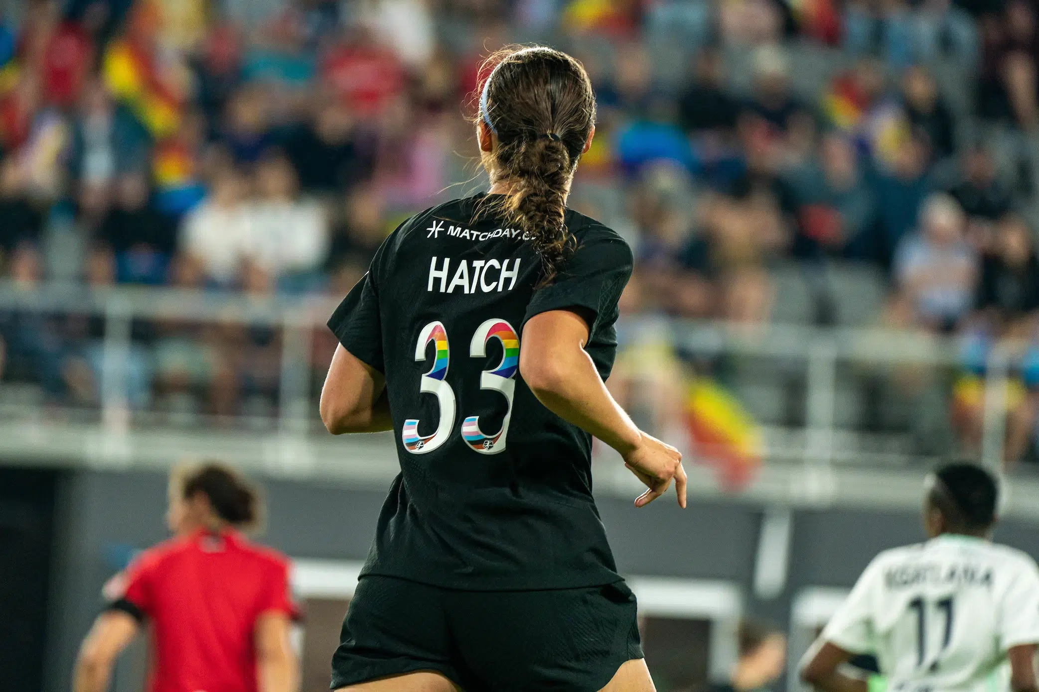 Ashley Hatch jogs away wearing an all black uniform with rainbow numbers. Her brown hair is in a braid.