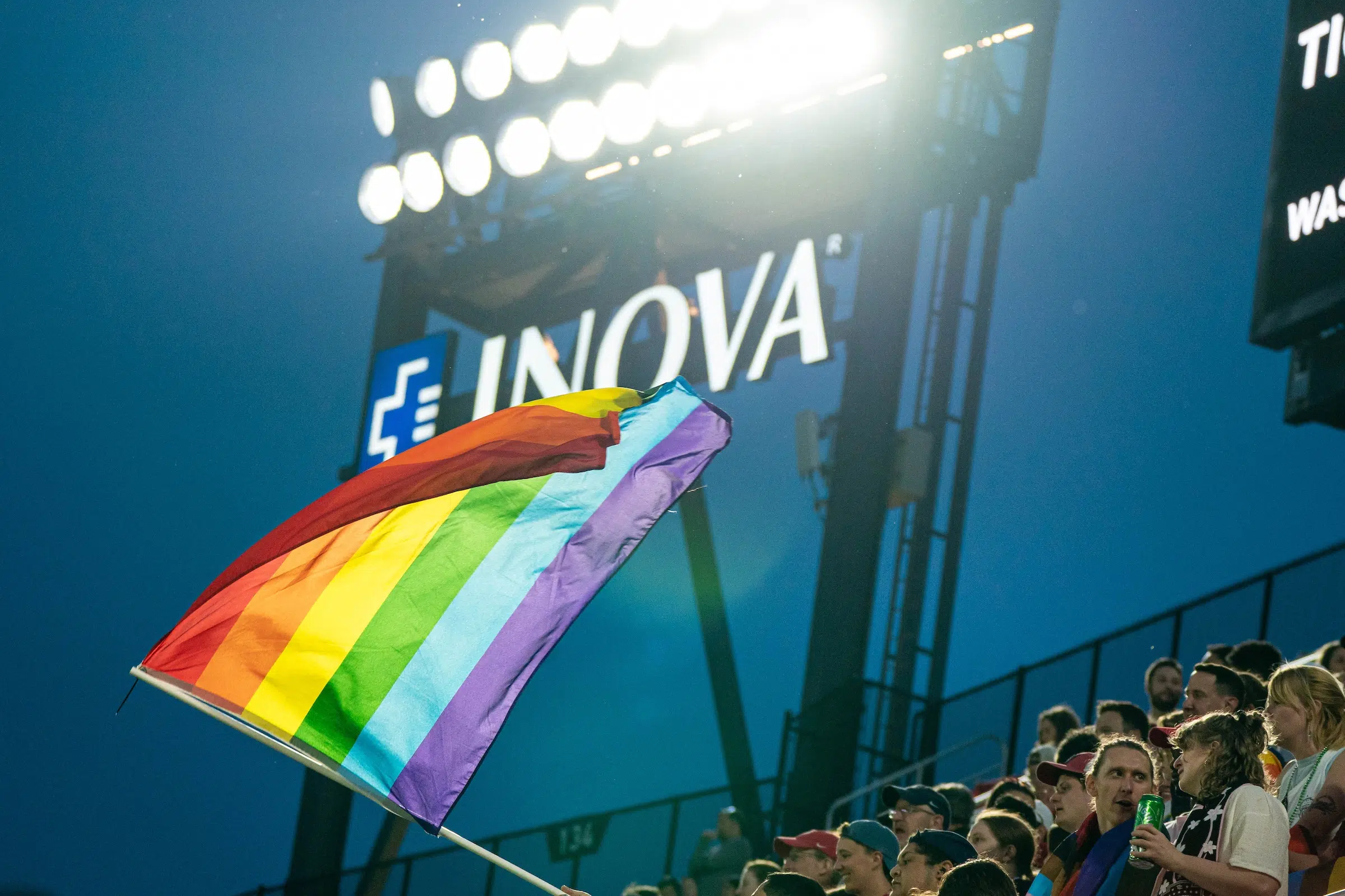 An LGBTQ+ rainbow flag is waved above a crowd of fans.