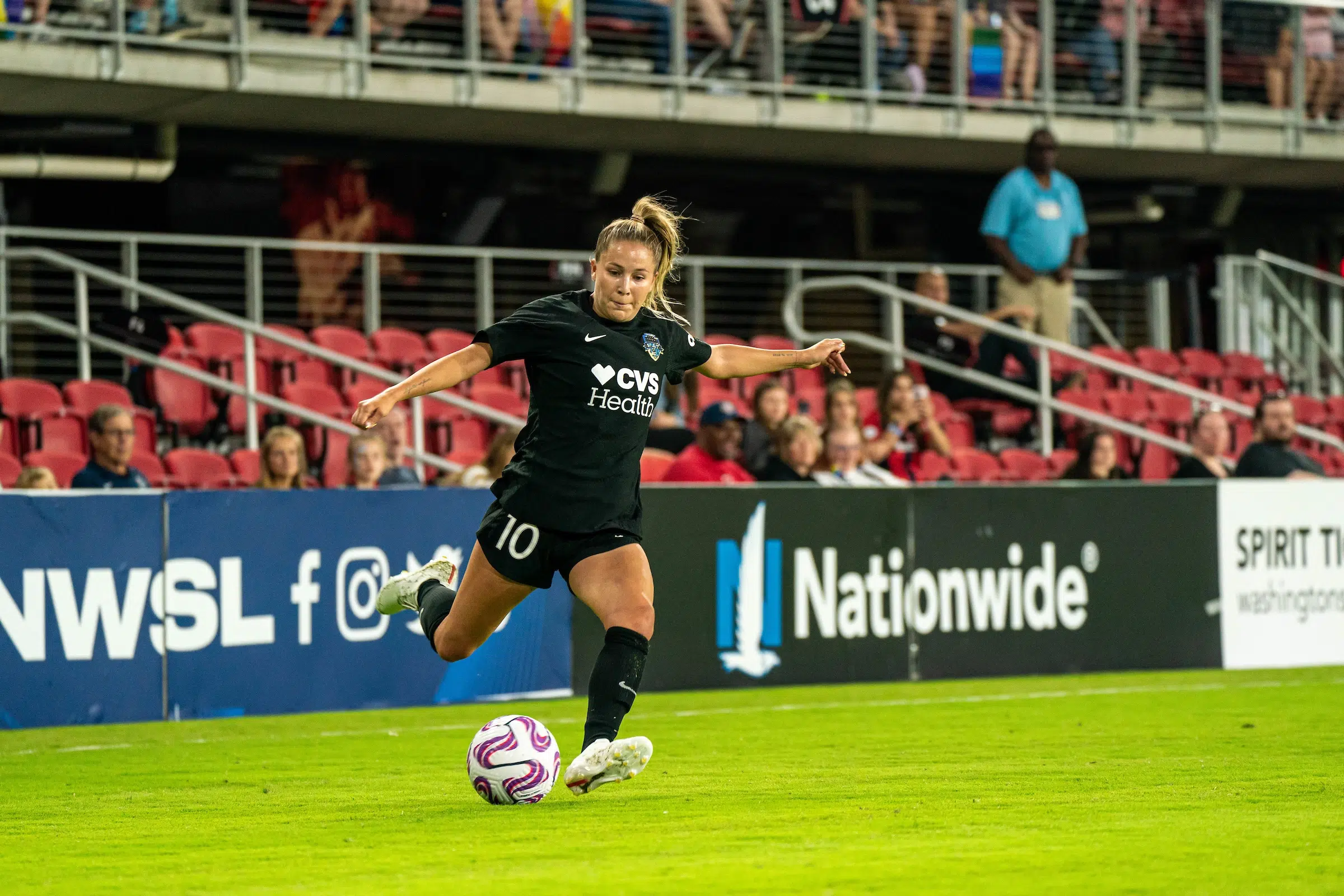 Ashley Sanchez in a black uniform winds up to cross a soccer ball into the 18-yard box.