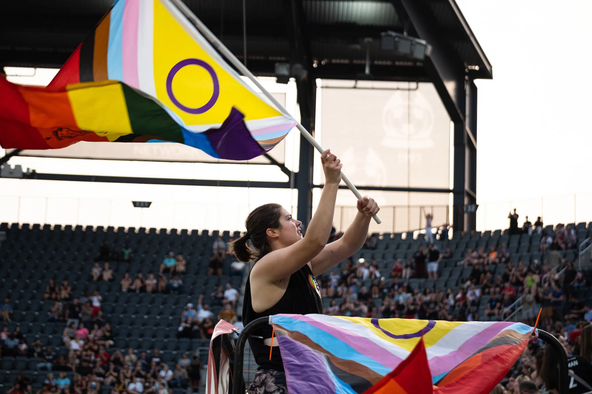 A fan in a black tank top waves an LGBTQ+ pride flag.