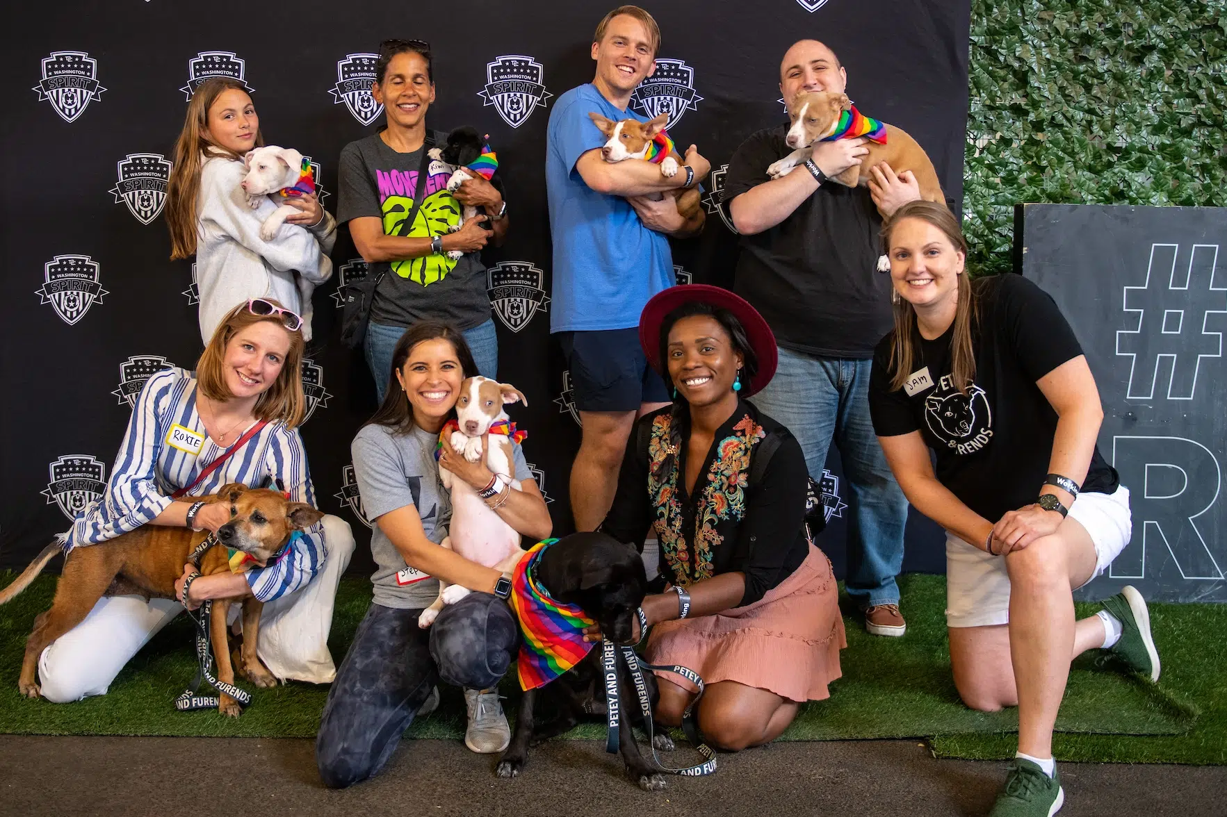 Eight fans pose with seven rescue dogs in rainbow bandanas.