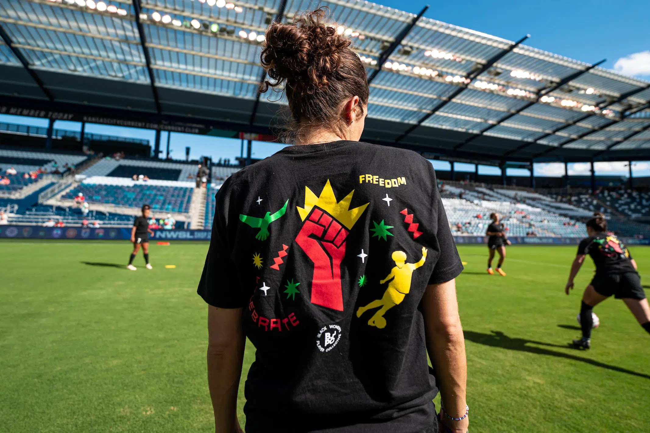The back of a black t-shirt featuring a red fist with a gold crown, a yellow silhouette of a soccer player and the word FREEDOM.