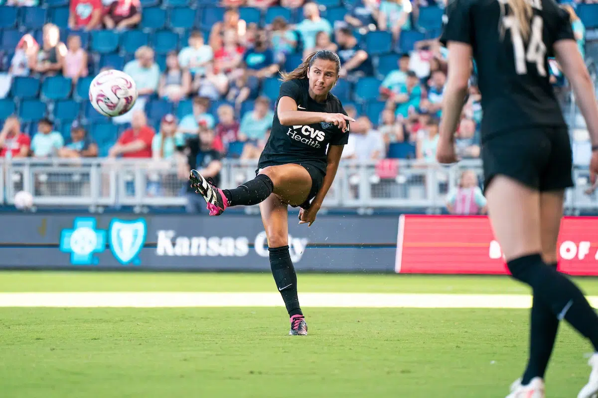 Sam Staab in an all black uniform kicks a soccer ball.