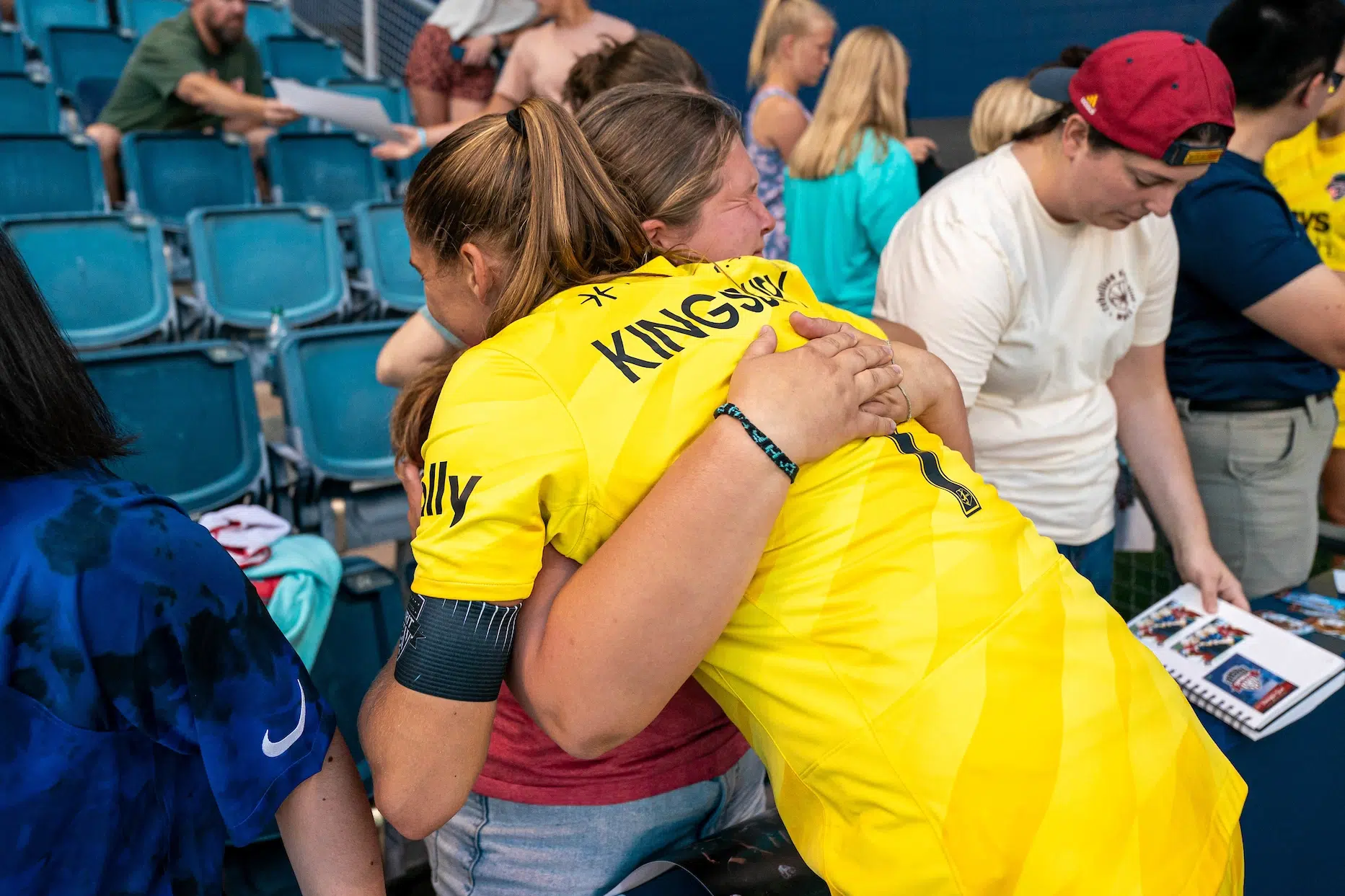 Aubrey Kingsbury in a yellow jersey hugs a fan in a red shirt who closes her eyes to hold in tears.