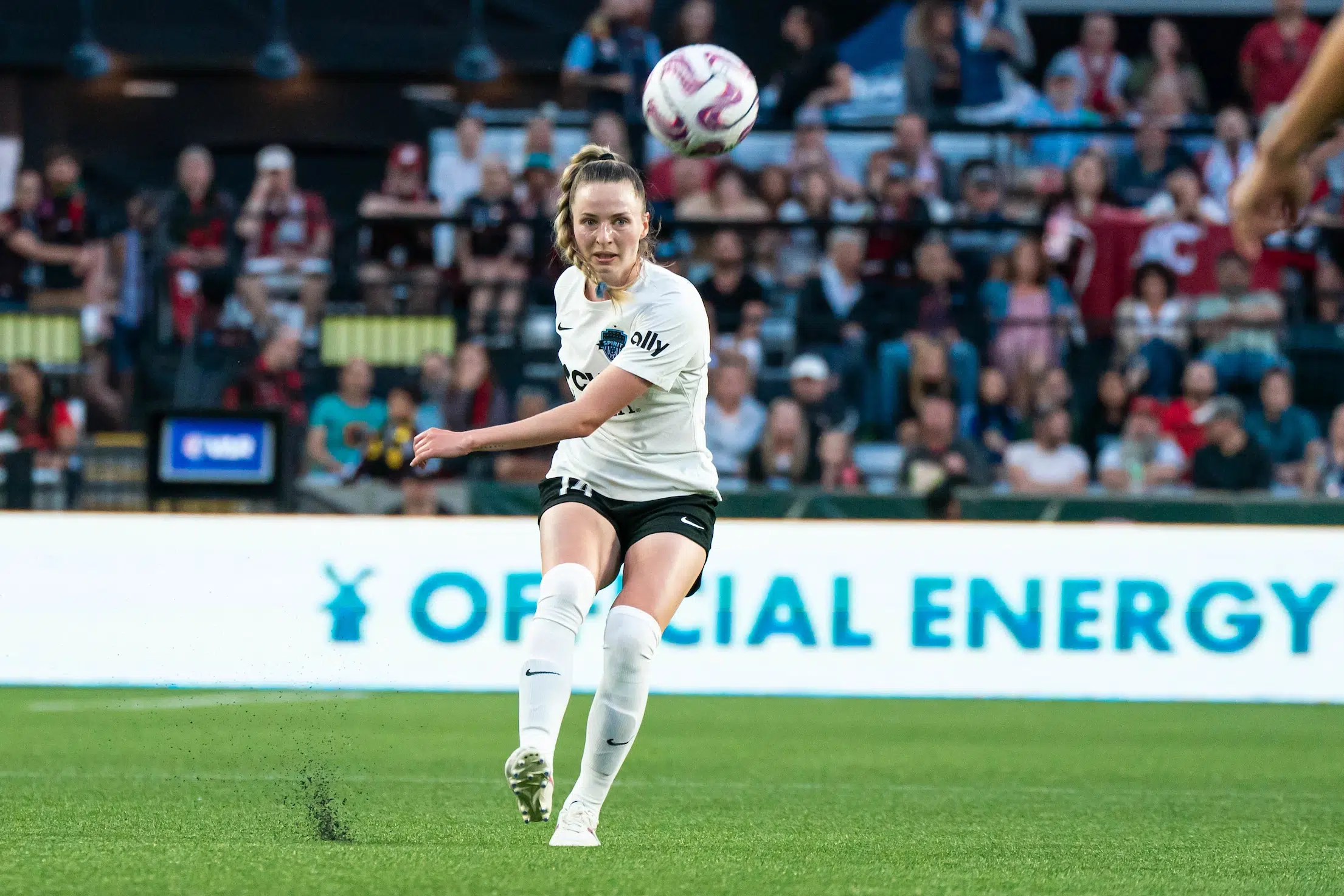 Gabby Carle in a white jersey, black shorts and white socks kicks a soccer ball.