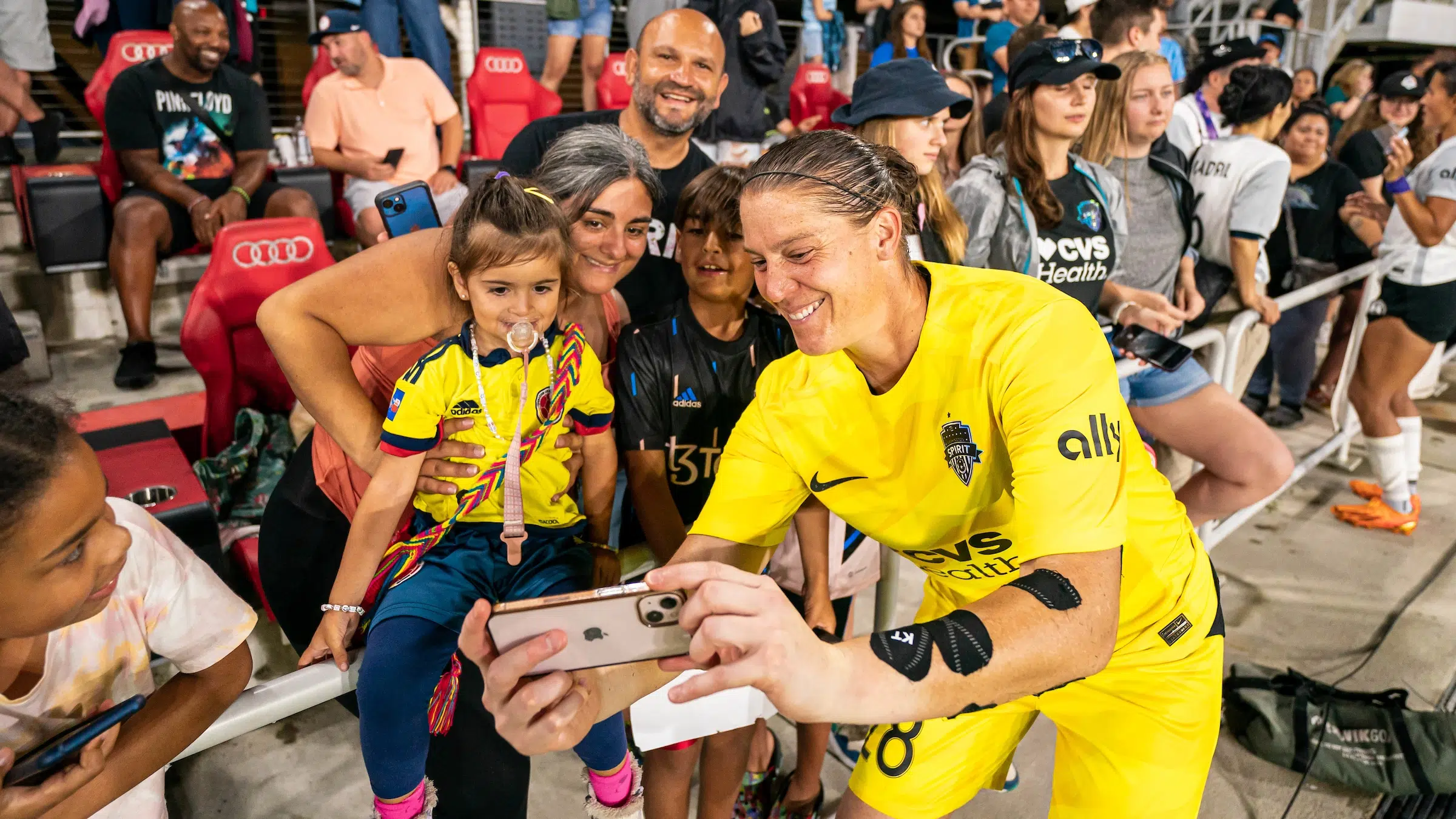 Nicole Barnhart in a yellow uniform takes a selfie on an iPhone with two young fans and their families.