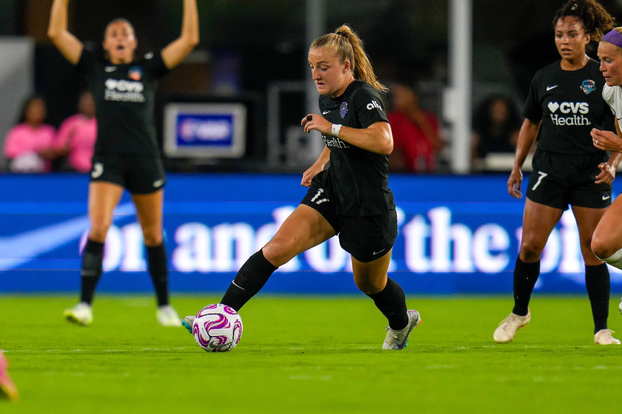 Nicole Douglas in a black uniform dribbles a soccer ball on a green field.