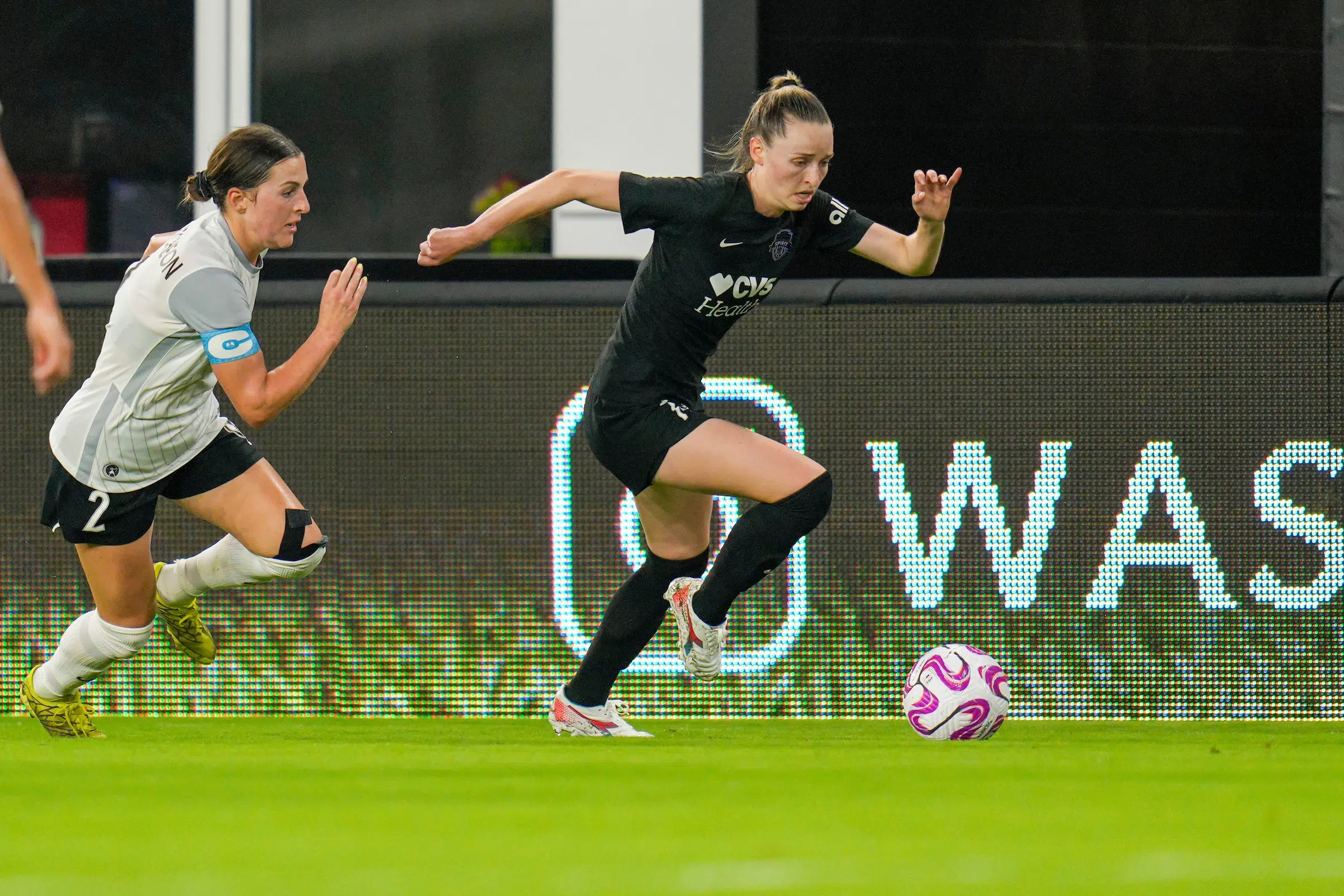 Gabby Carle in a black uniform dribbles a soccer ball passed a defender.