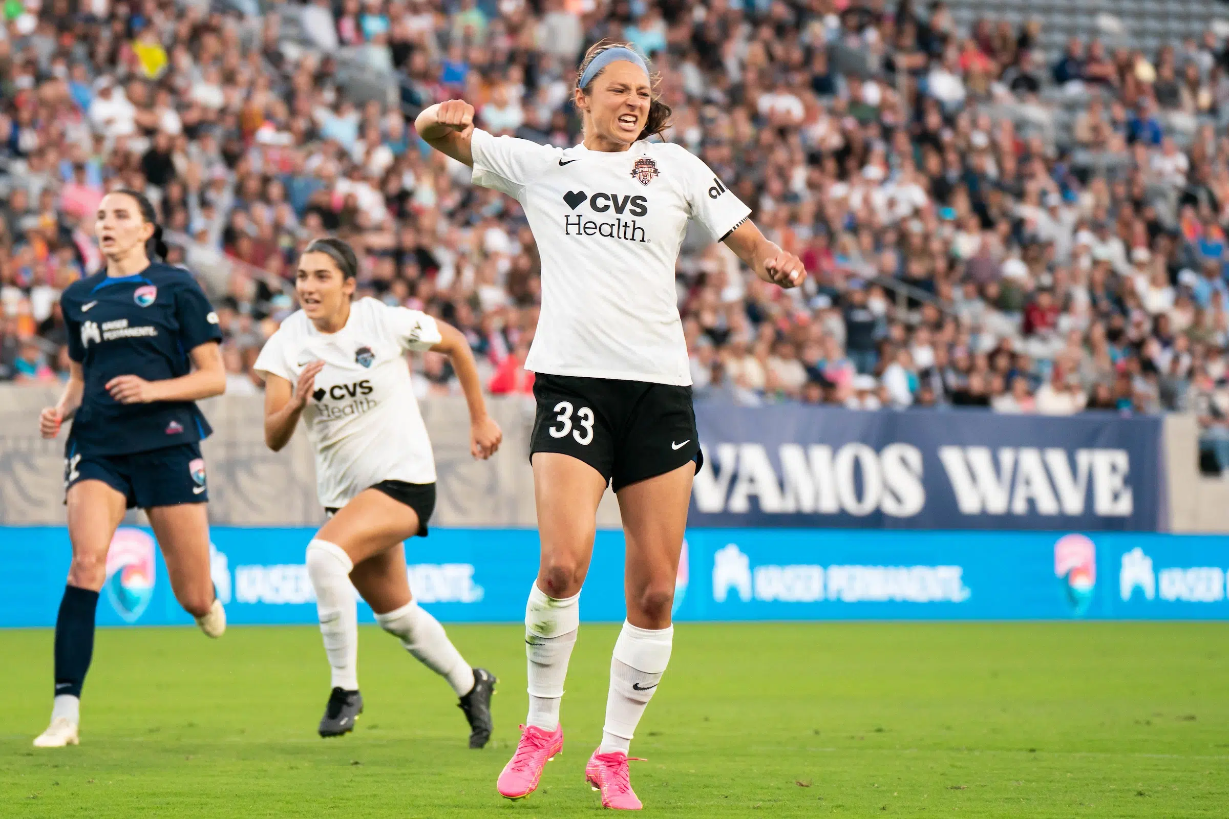Ashley Hatch in a white top, black shorts, white socks and pink cleats pumps her fist in celebration.