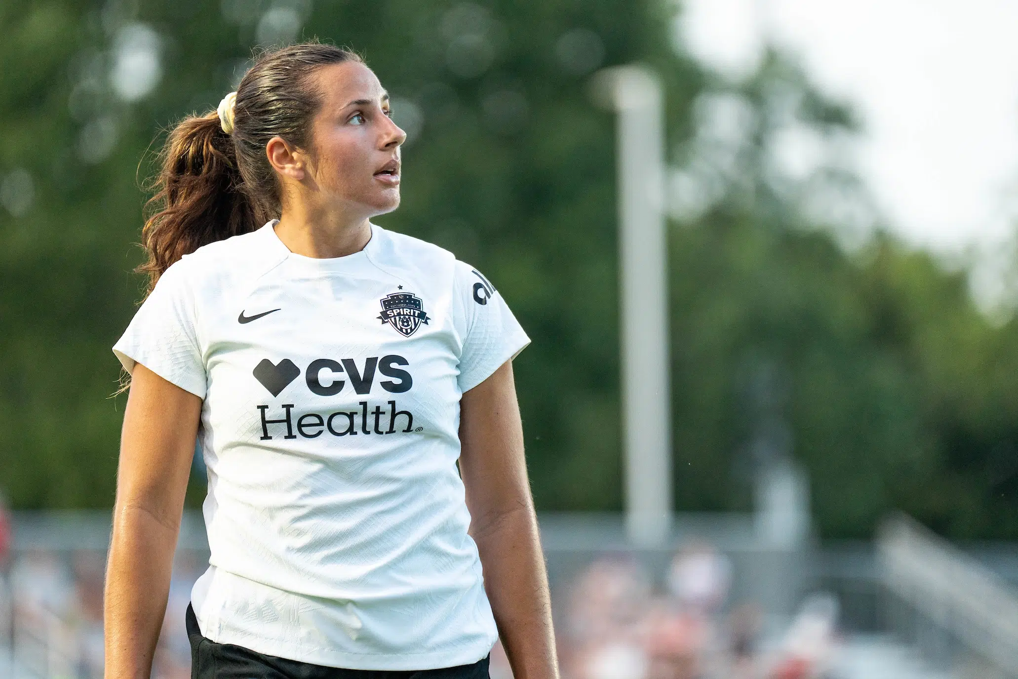 Sam Staab in a white top and her brown hair in a ponytail looks to her left on a soccer field.