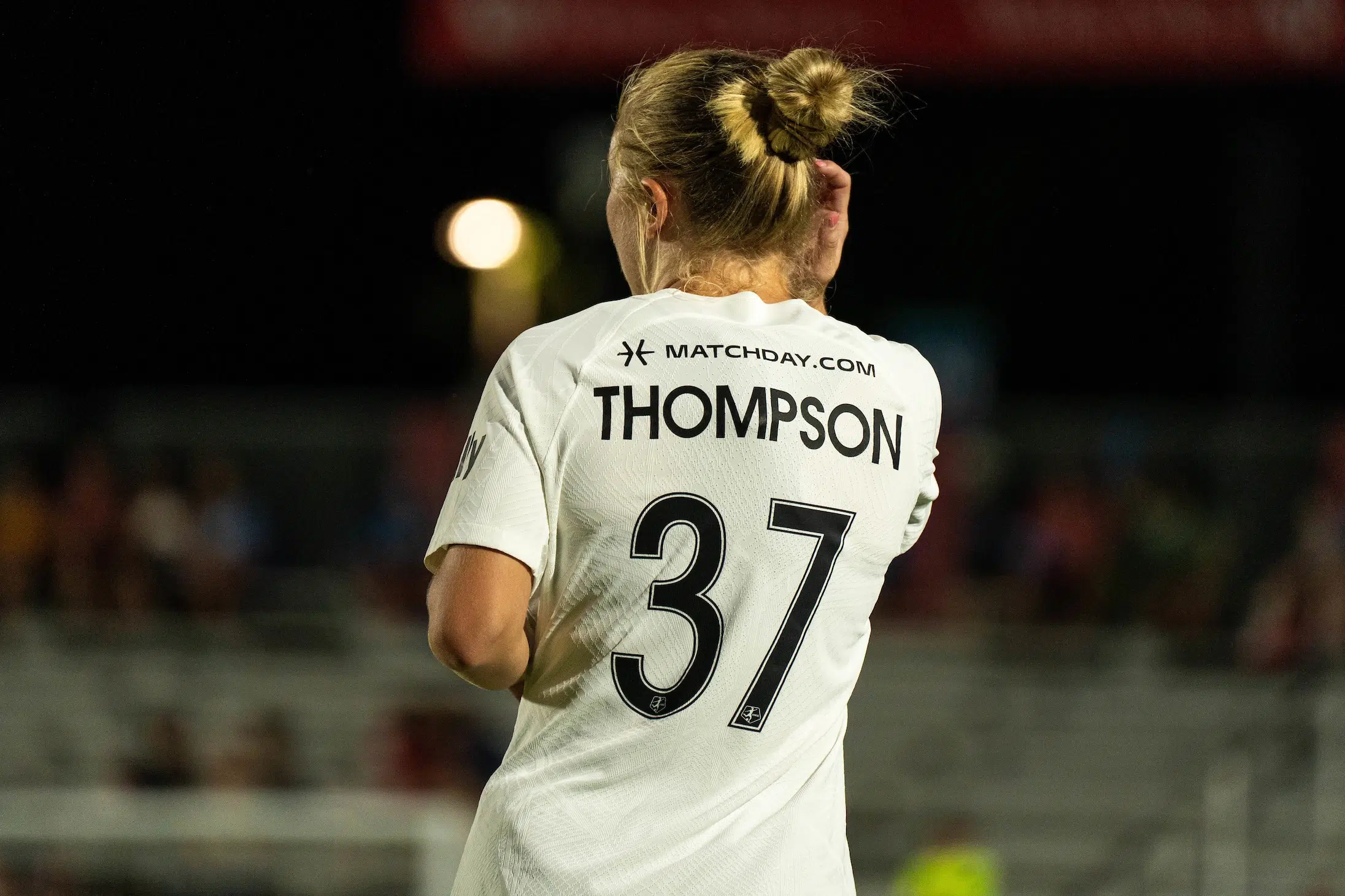 The back of Jordan Thompson's white uniform with the number 37. Her blonde hair is in a bun.