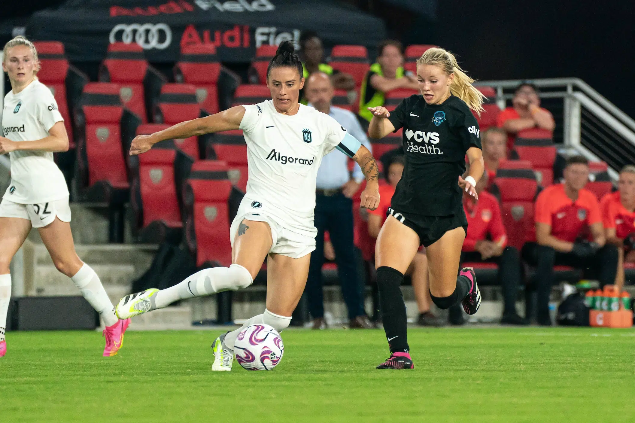 Chloe Ricketts in a black uniform defends Ali Krieger in a white uniform who dribbles a soccer ball.