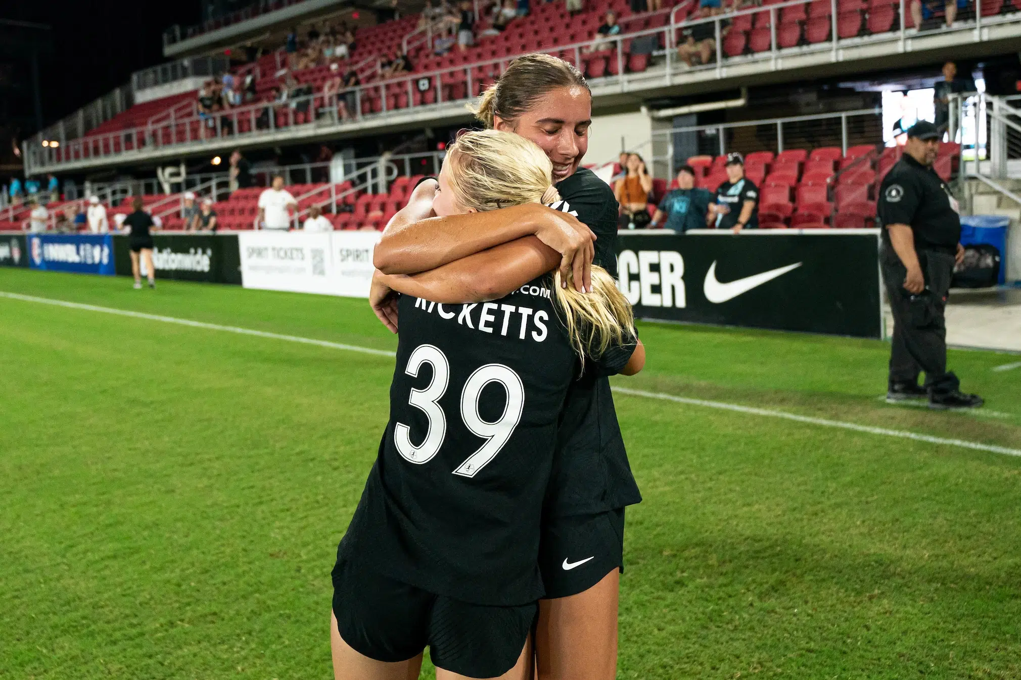 Mariana Speckmaier closes her eyes and hugs Chloe Ricketts on a soccer field. Both are in all black uniforms.