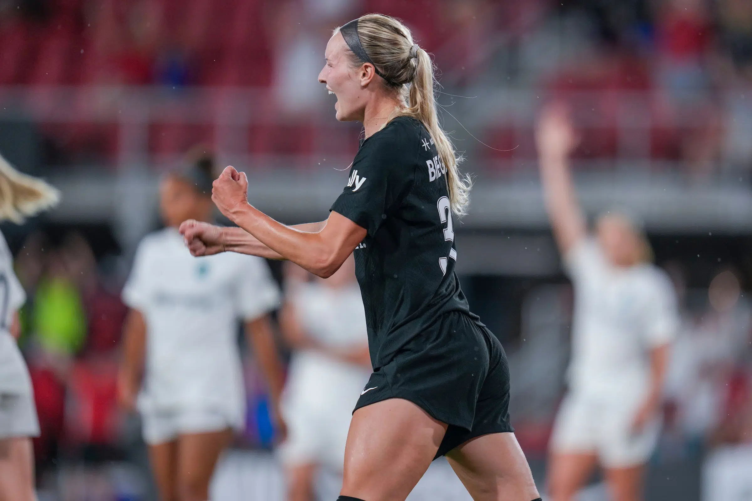 A blonde soccer player in an all black pumps her fist in excitement.