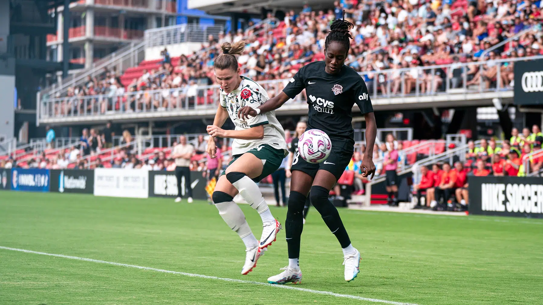 Ouleymata Sarr in an all black uniform looks to control the soccer ball as a player in a white top and green shorts tries to defend.