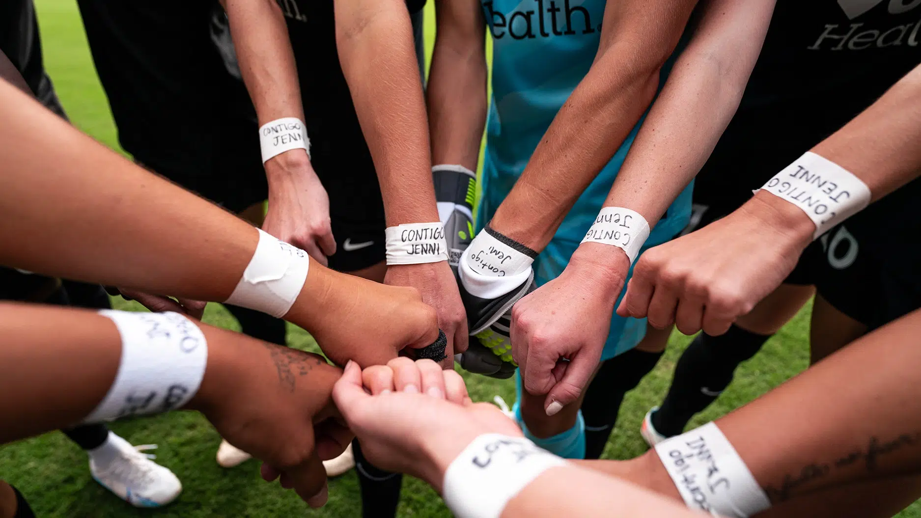 A group of players put their fists together showing their wrists all have white athletic tape around them with the words 