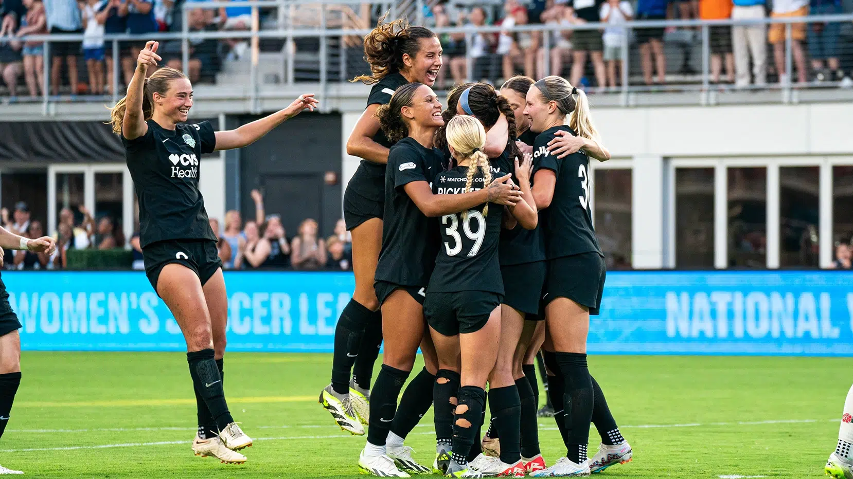 A group of Spirit players in black uniform hug and jump in celebration.