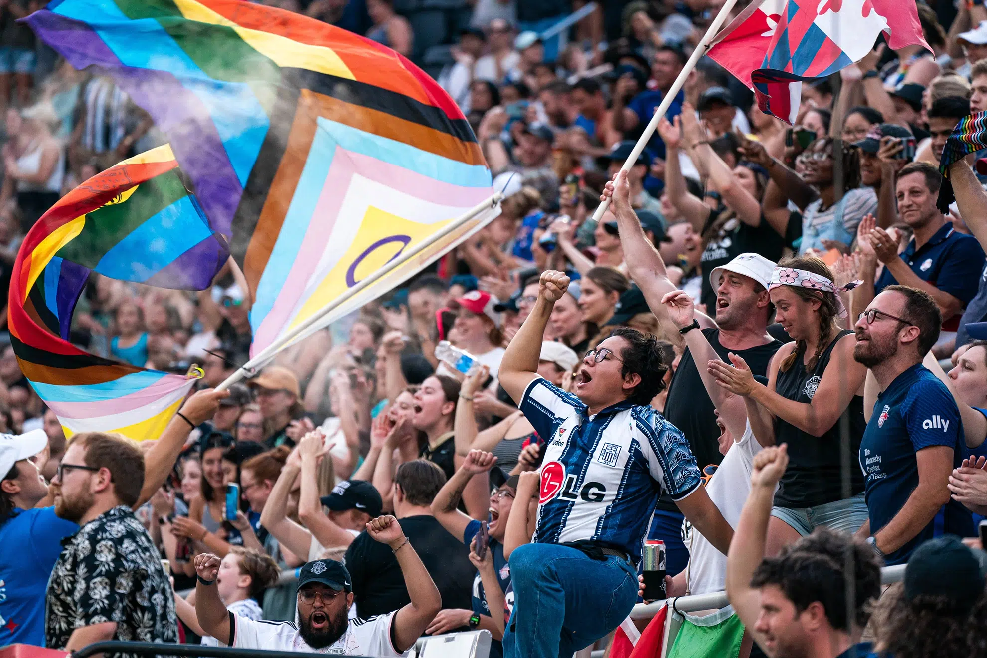 Fans yell and pump their fist in the air as an LGBTQ+ flag is waved.
