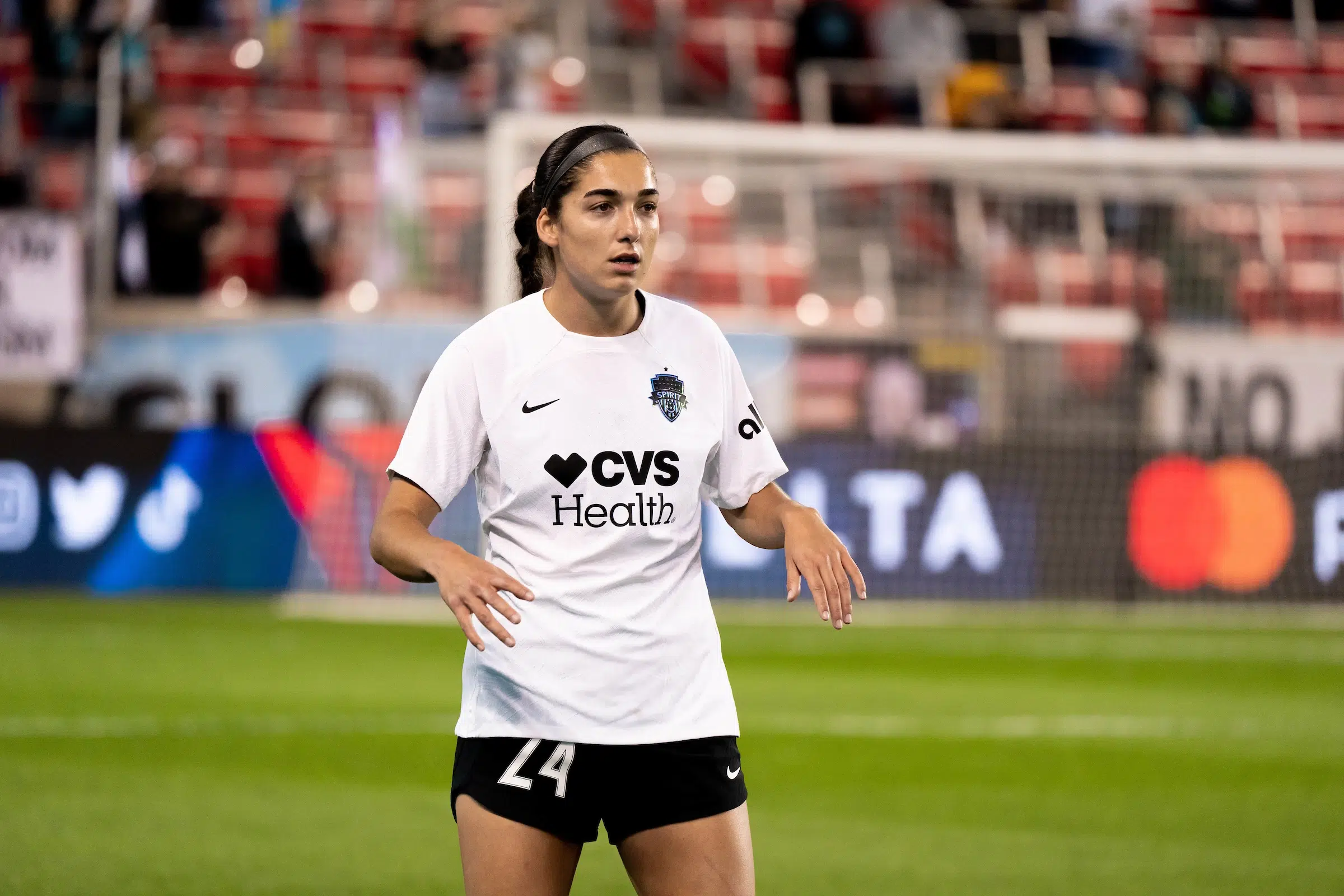 Lena Silano in a white uniform and black shorts stands on a soccer field waiting for the ball to be put back in play.