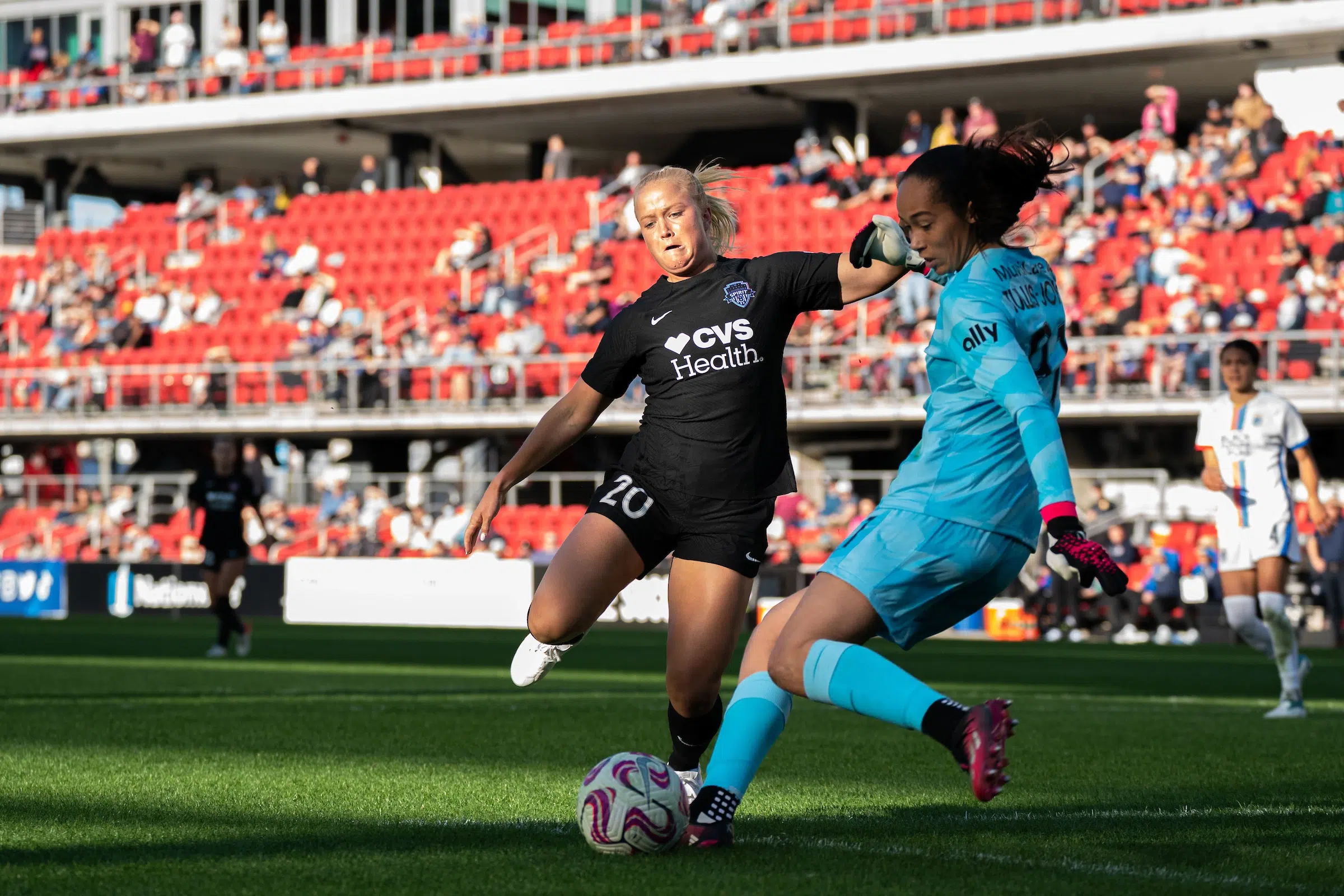 Civana Kuhlmann in a black uniform runs at a goalie in a bright uniform who is attempting to kick a soccer ball.