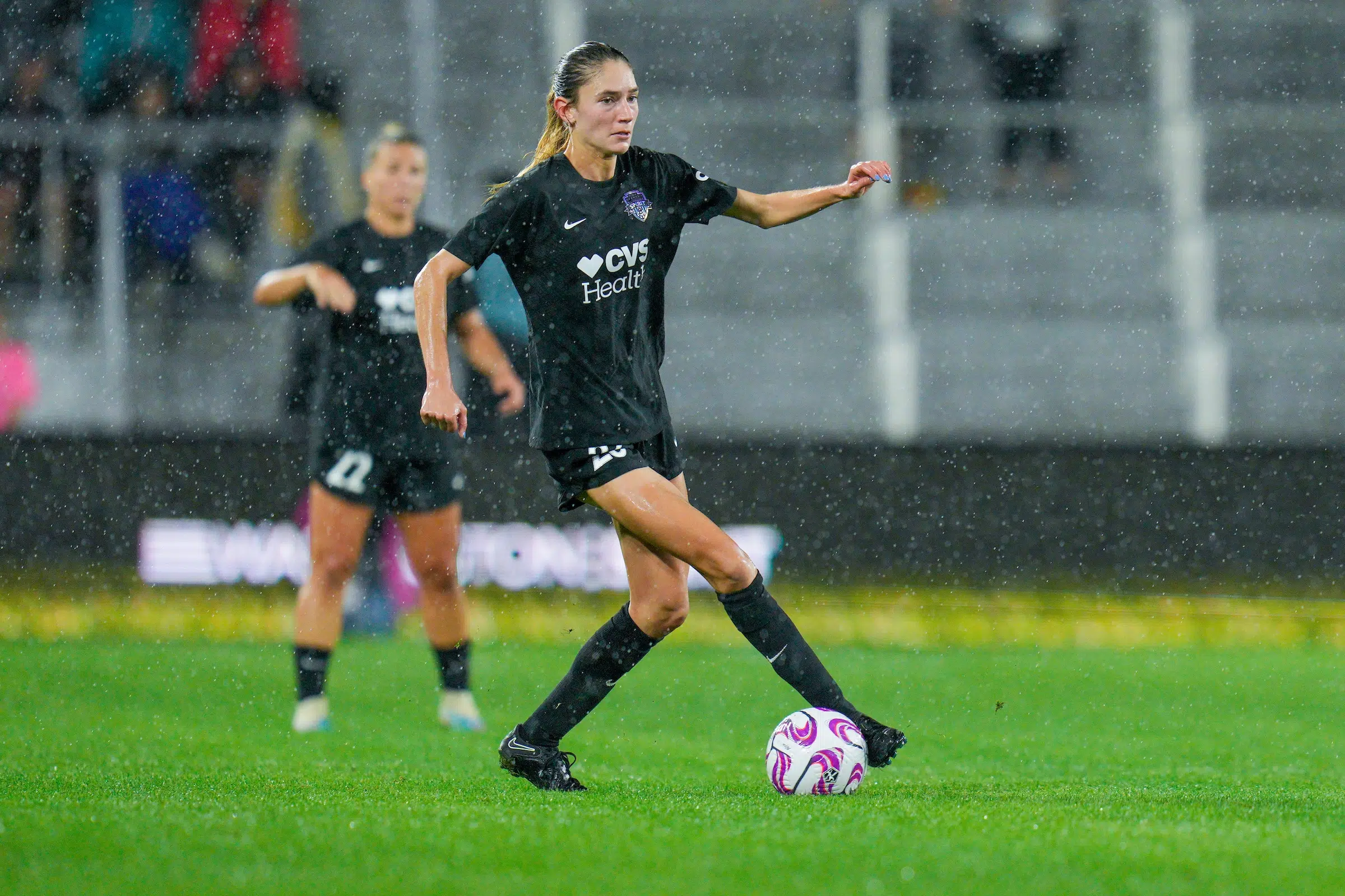 Paige Metayer in an all black uniform dribbles a soccer ball as rain pours down.