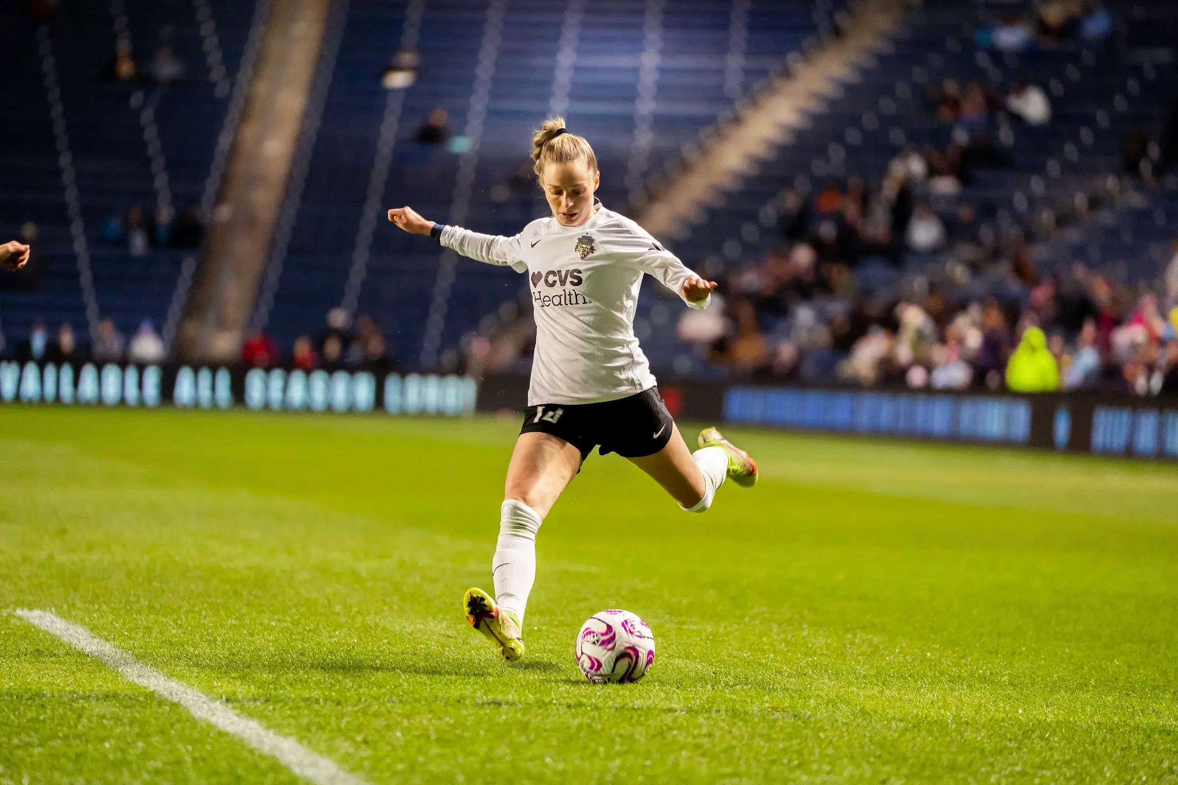 Gabby Carle in a long-sleeved white top, black shorts and white socks kicks a soccer ball.
