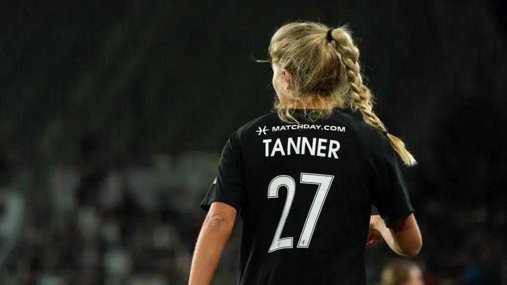 Riley Tanner faces away with her blonde hair in a braid, wearing a black uniform with her last name and the number 27 on the back.