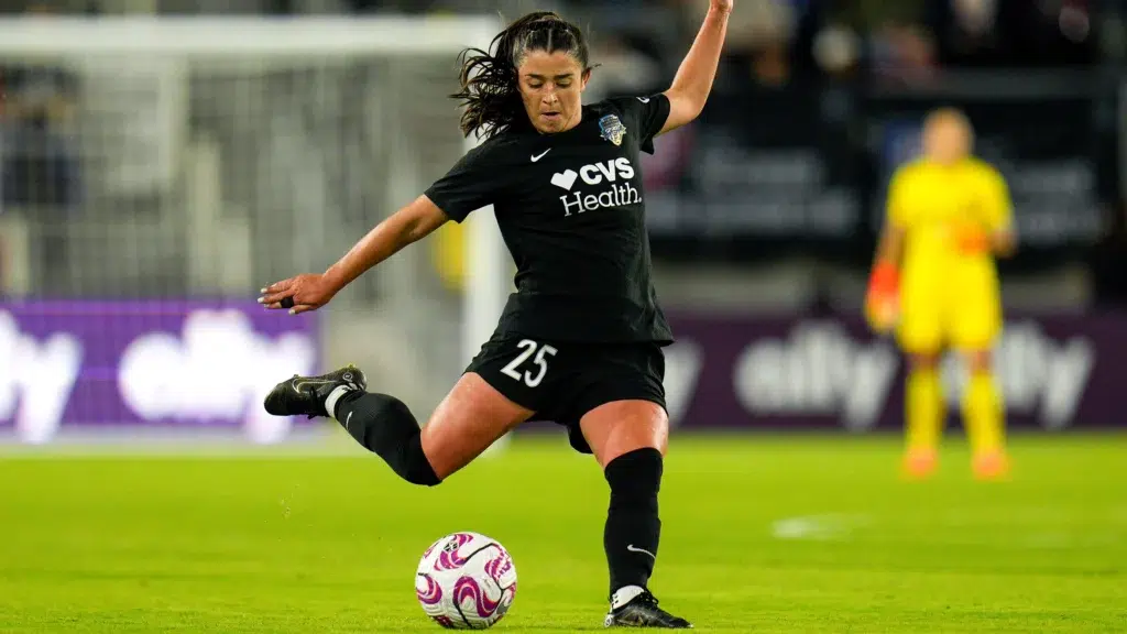 Marissa Sheva in a black Spirit uniform winds up to kick a soccer ball.