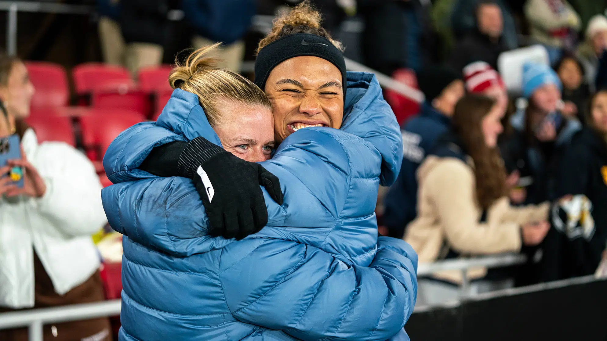 Anna Heilferty and Trinity Rodman hug each other while wearing steel blue puffy jackets.