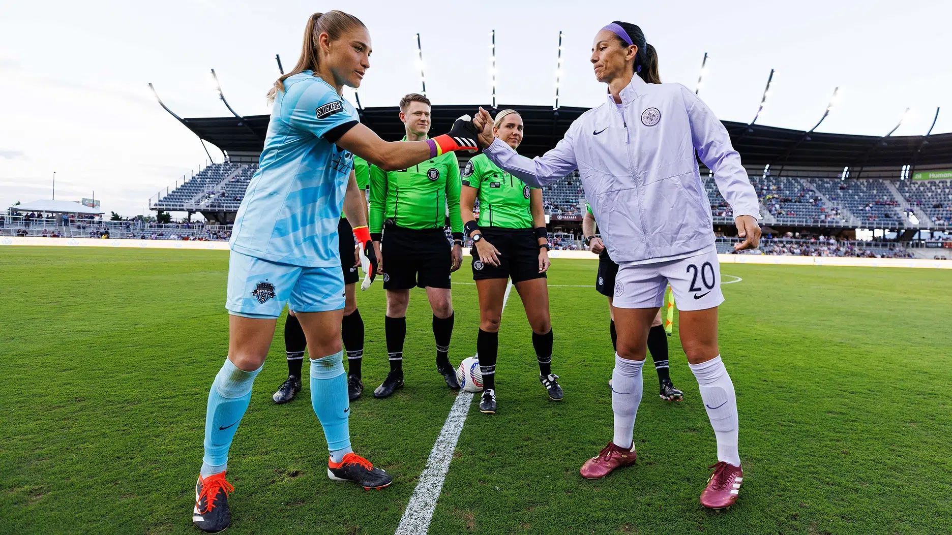 Aubrey Kingsbury in a blue kit gives a fist bump to a Racing Louisville captain as three refs in bright green stand in the background.