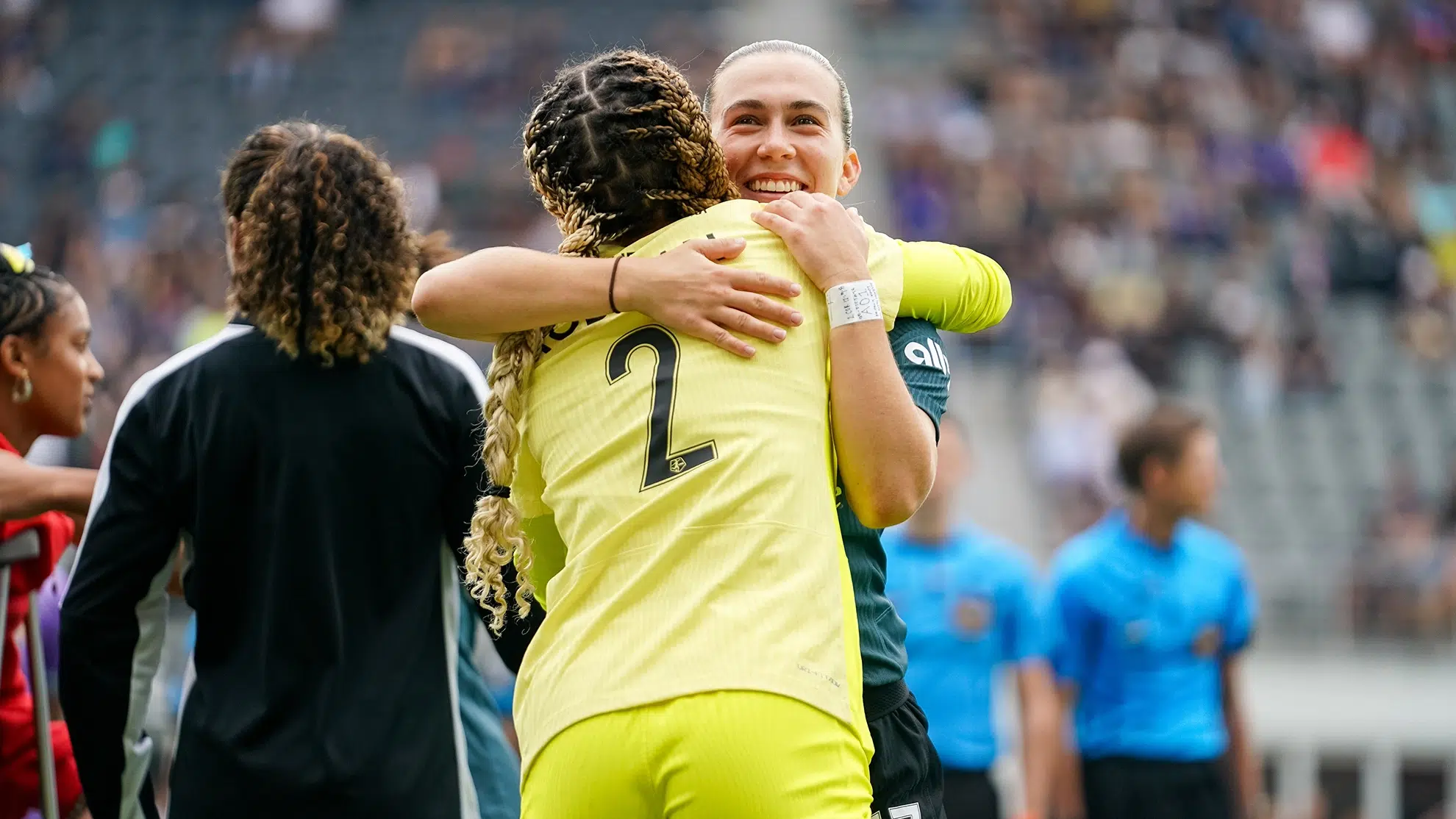 Trinity Rodman in a yellow kit hugs Sam Coffey in a gray kit.