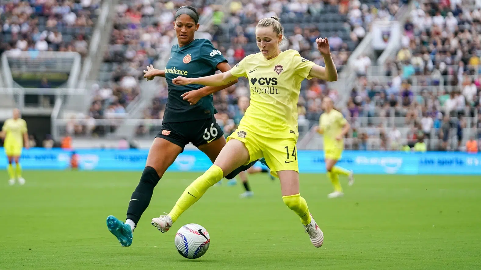 Gabrielle Carle in a yellow kit keeps the ball away from a Portland Thorns attacker in gray.