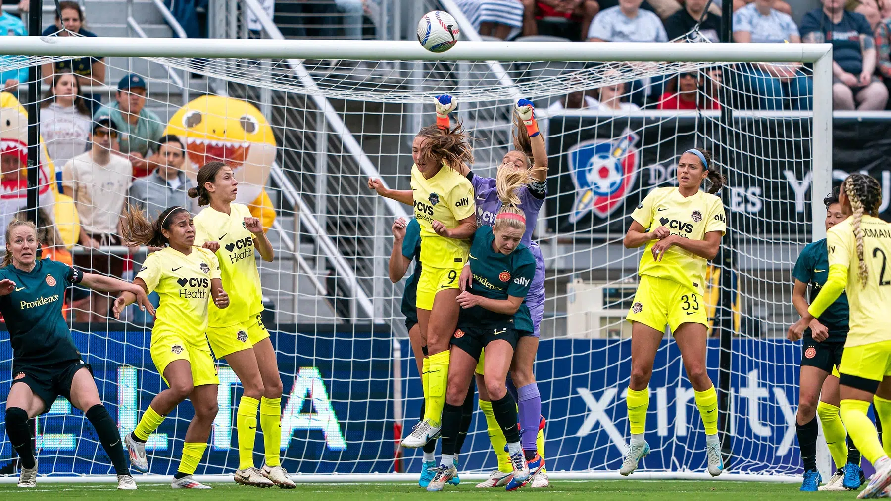 A group of players from two teams jump up for a ball in front of the goal.