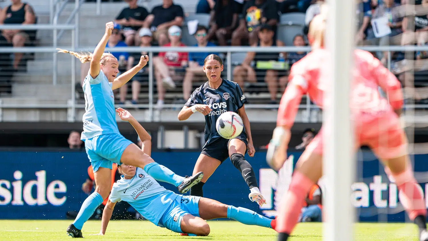 Trinity Rodman shoots the ball passed two Houston Dash defenders in blue kits.