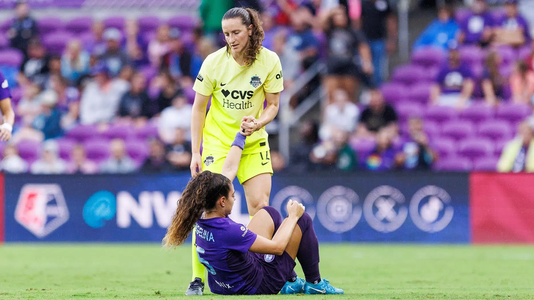 Andi Sullivan in yellow helps up an Orlando Pride player in purple.