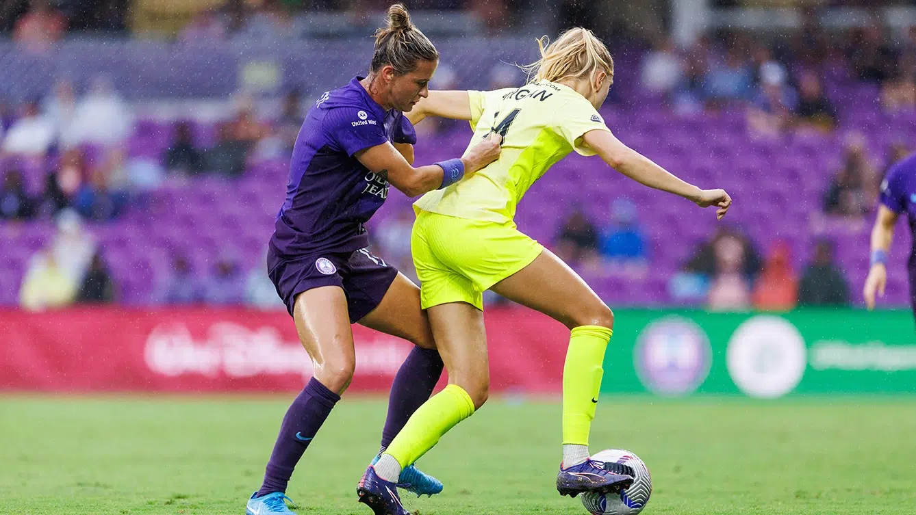 Esme Morgan in yellow keeps the ball away from an Orlando Pride player in purple.