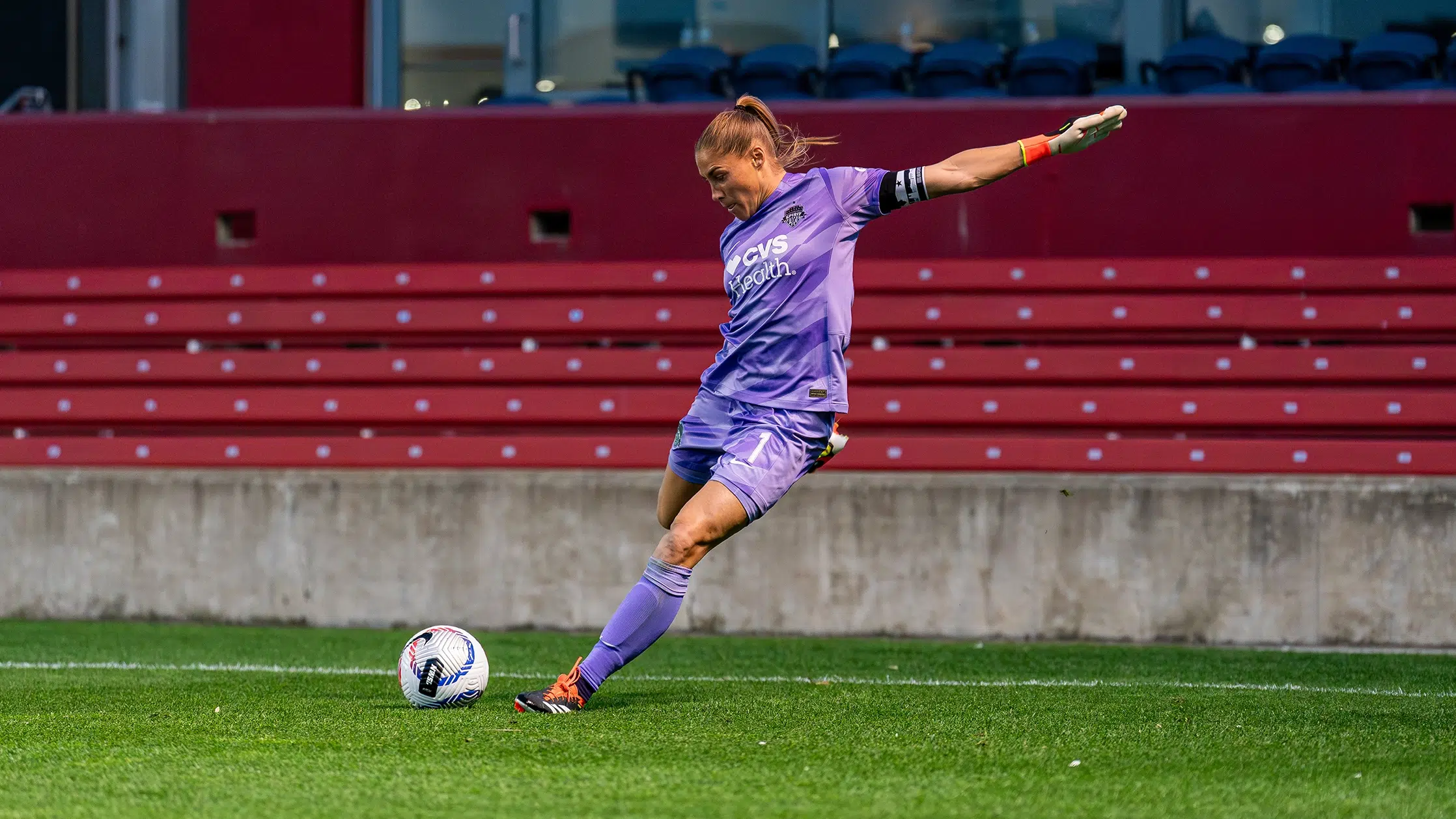 Aubrey Kingsbury in an all-purple kit winds up to kick a soccer ball.